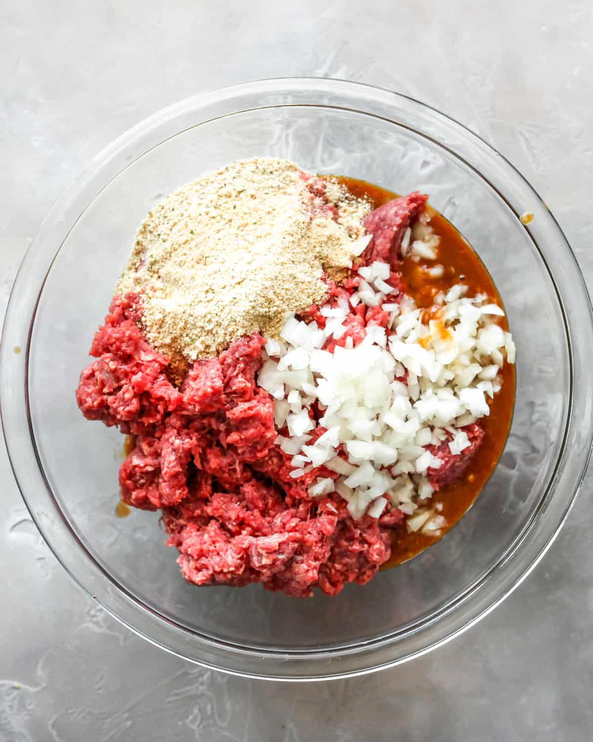How to Make Meatloaf - adding meat, breadcrumbs, spices and onions to the wet mixture in a glass bowl before mixing