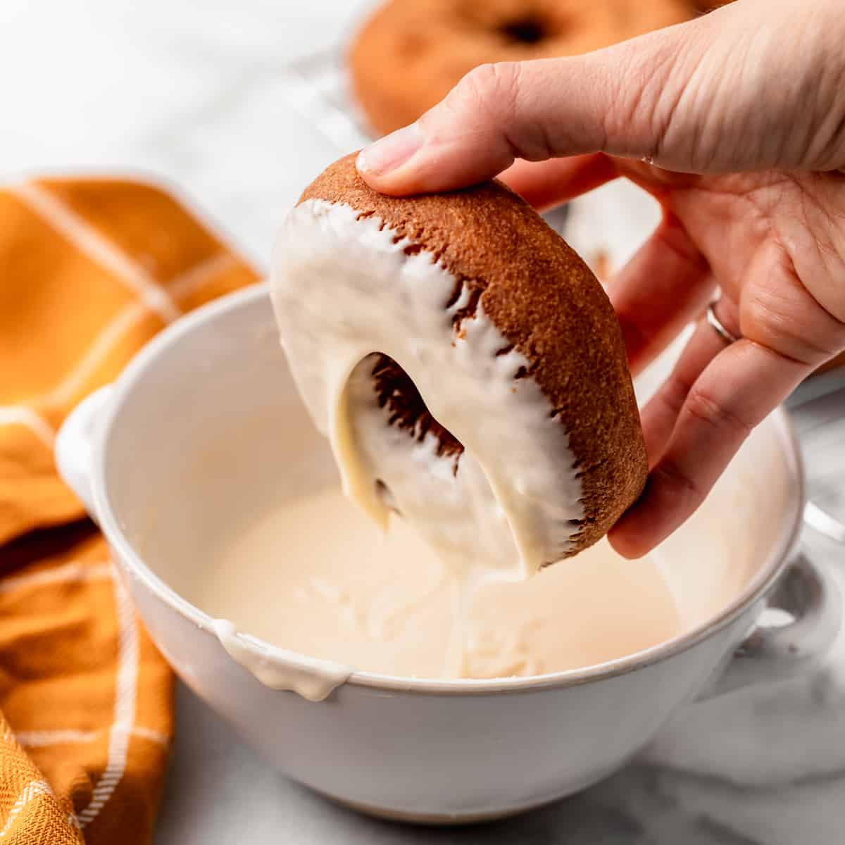 a donut being dipped in a bowl of Maple Glaze