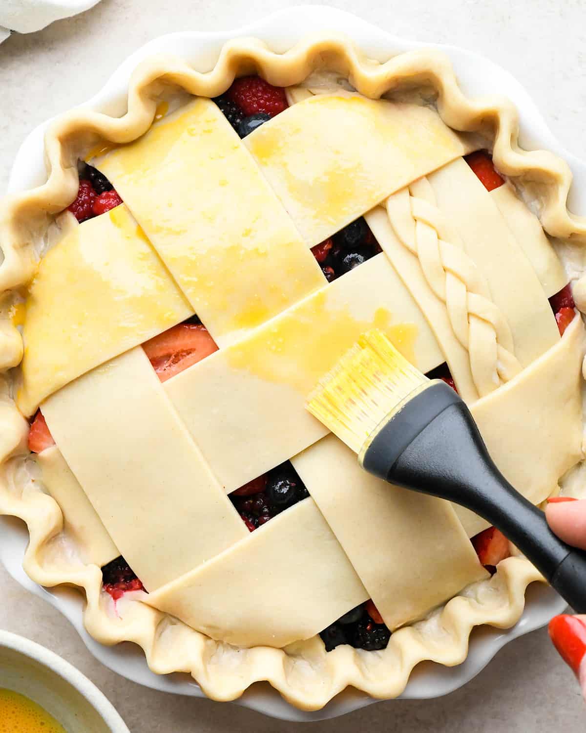 brushing egg wash over mixed berry pie crust