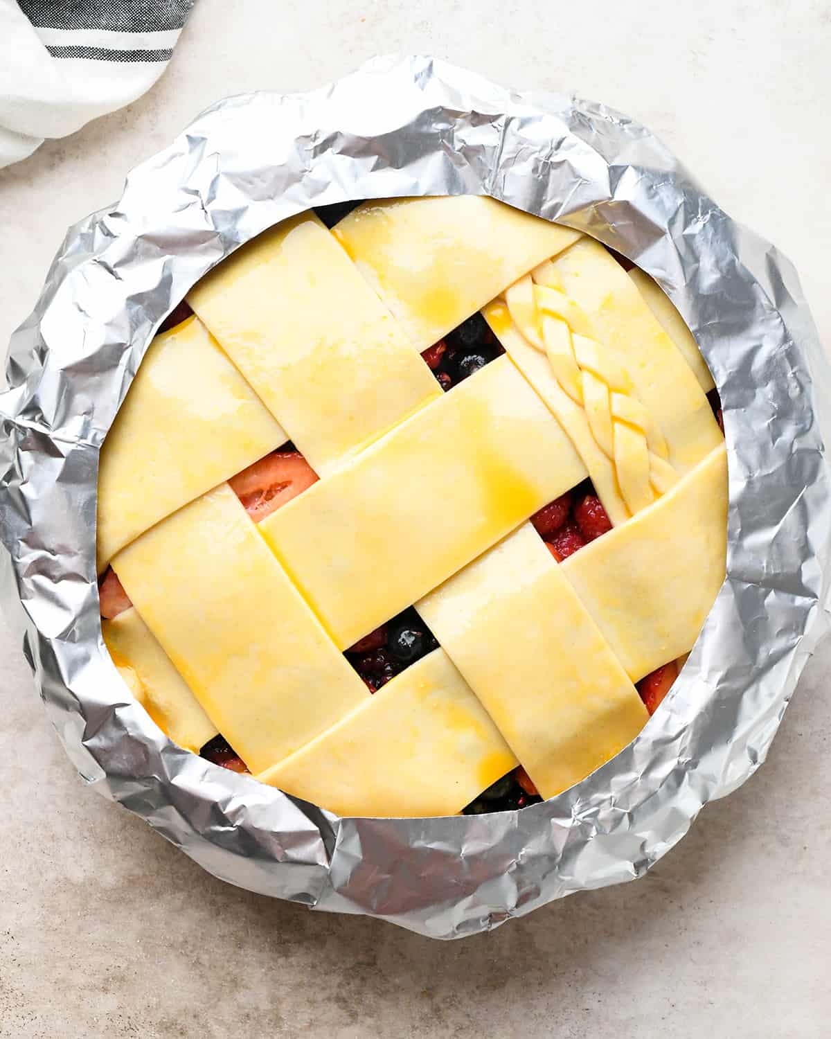 mixed berry pie with egg wash before baking with a pie crust shield around the edges