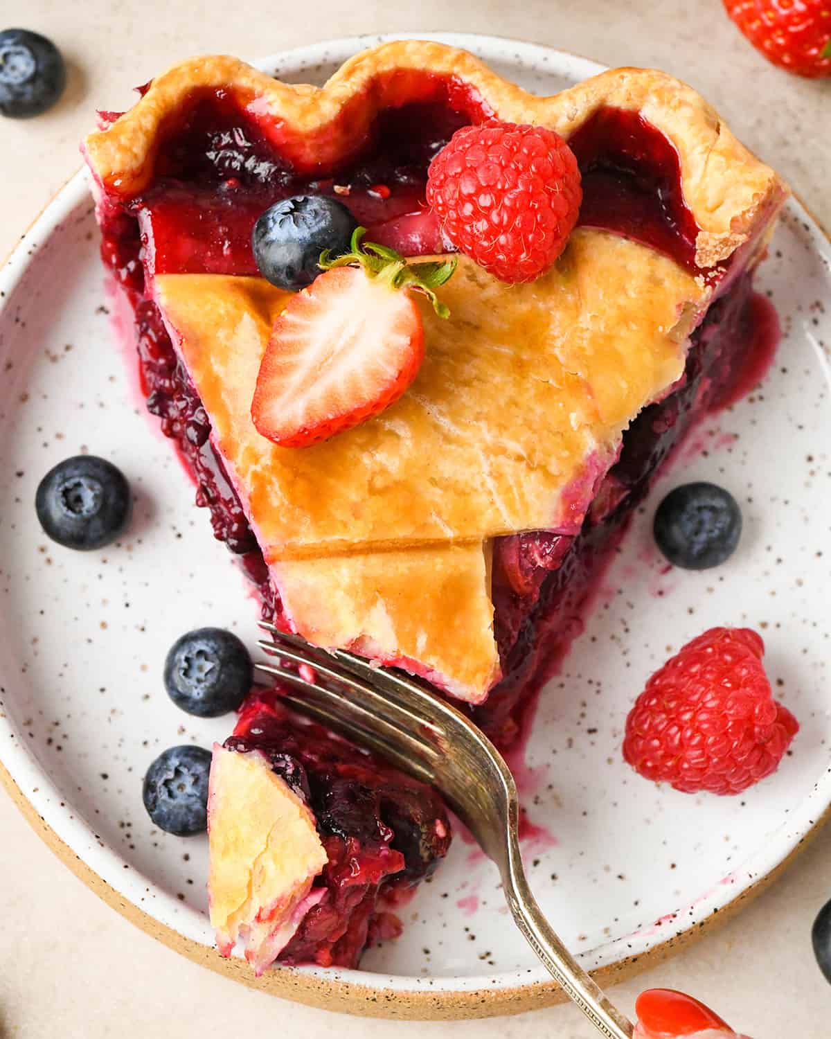 a slice of Mixed Berry Pie on a plate with a fork taking a bite