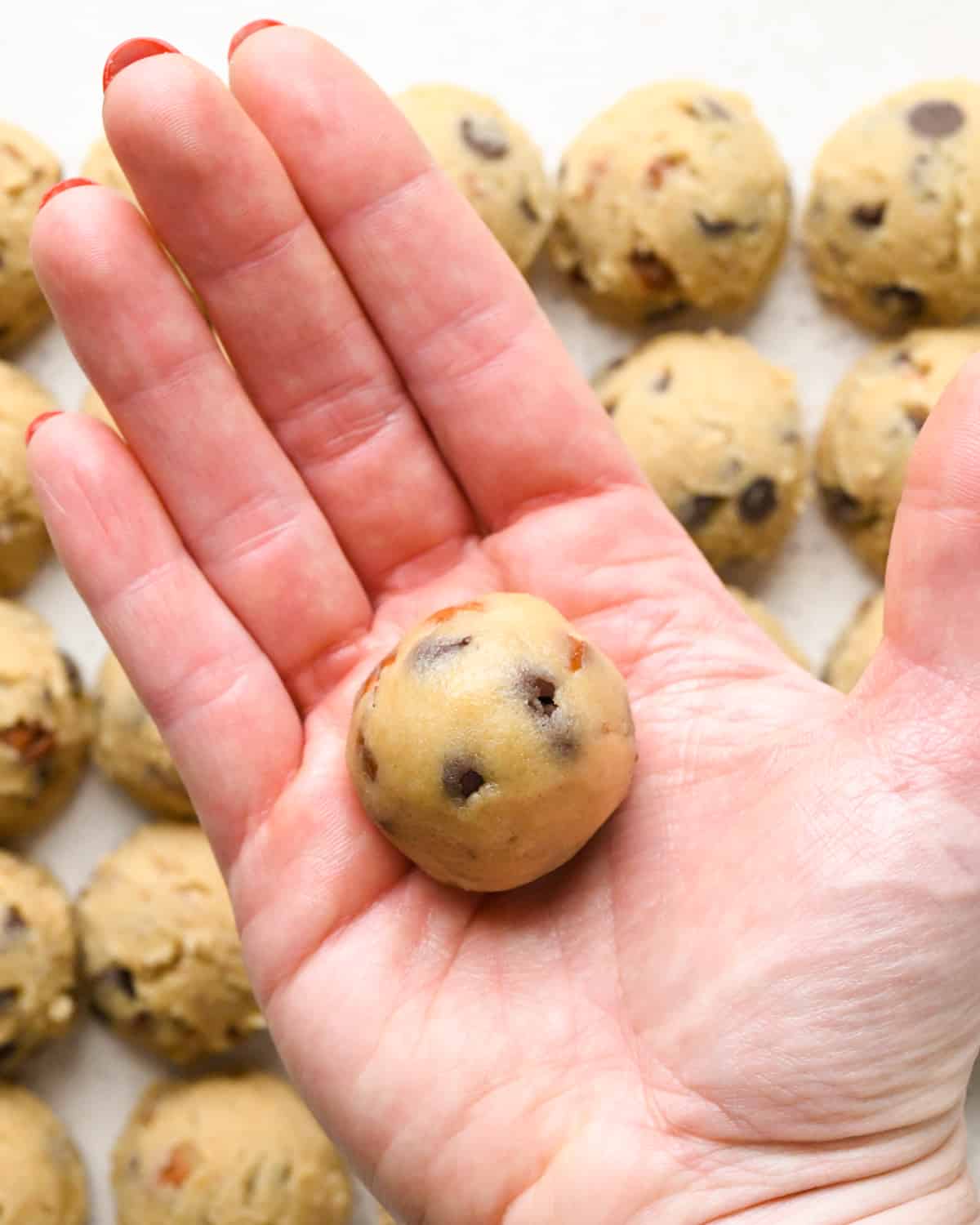 pecan chocolate chip cookie dough being rolled into a ball