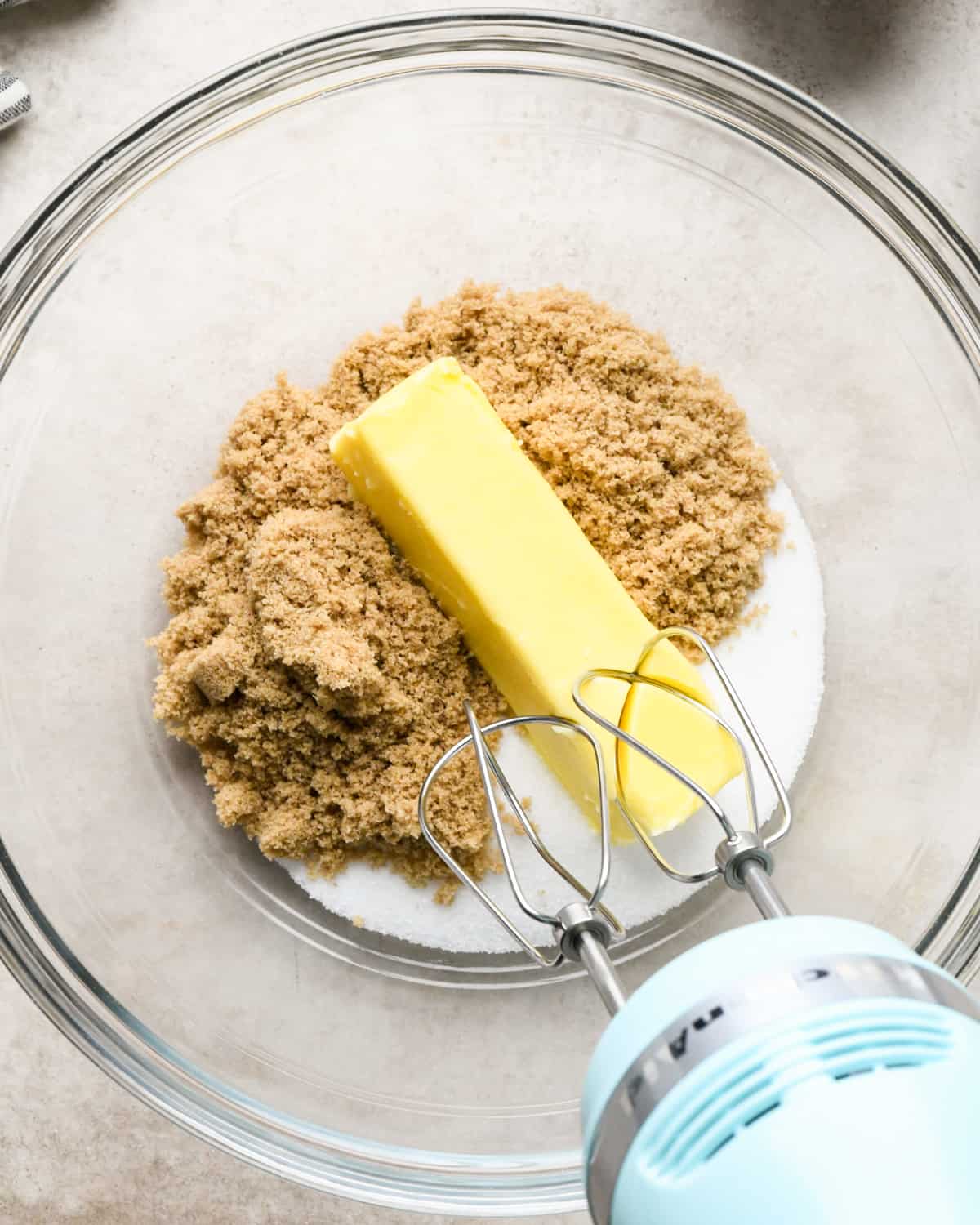 butter, white sugar and brown sugar in a bowl with a handheld mixer before mixing