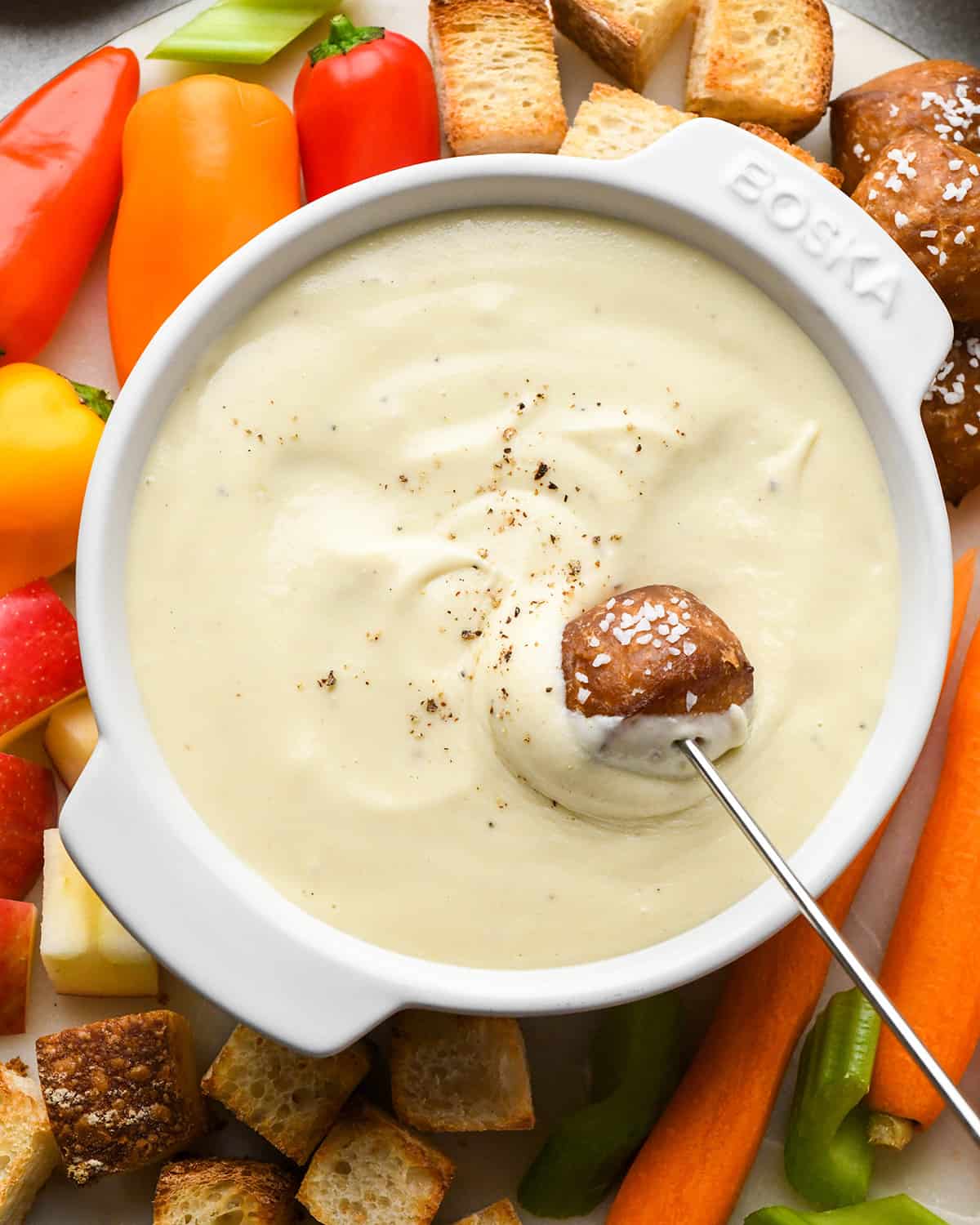 a soft pretzel bite being dipped into a bowl of Cheese Fondue