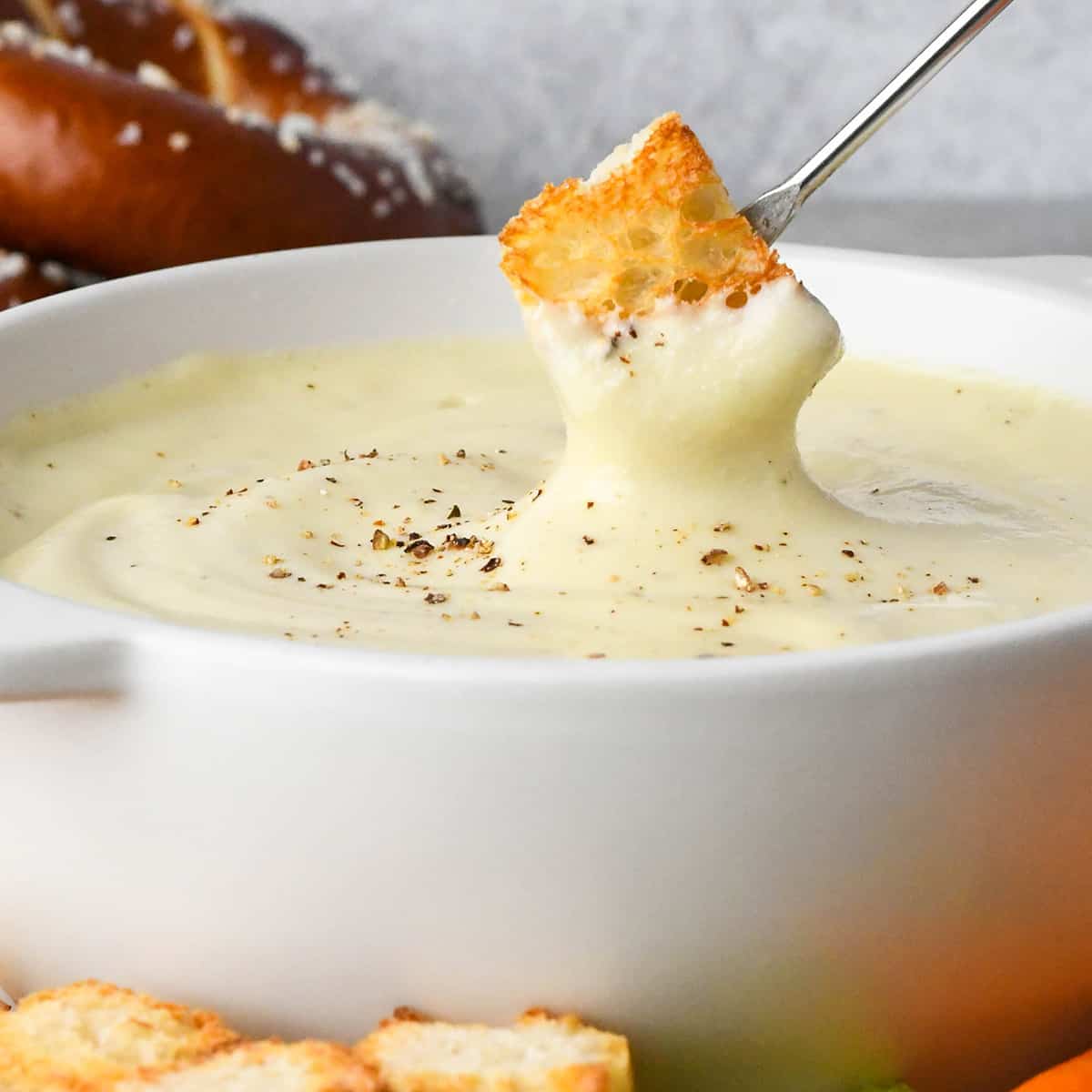 up close photo of a piece of bread being dipped into Cheese Fondue