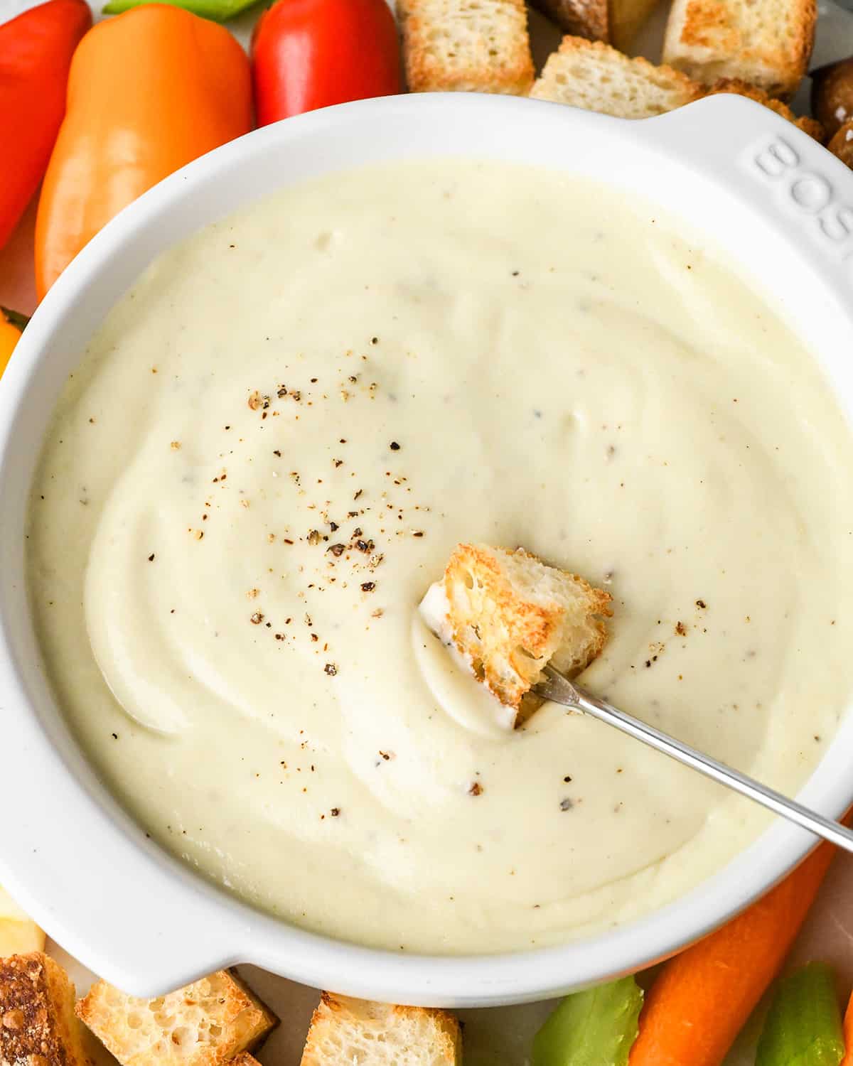 a piece of bread being dipped into a bowl of cheese fondue