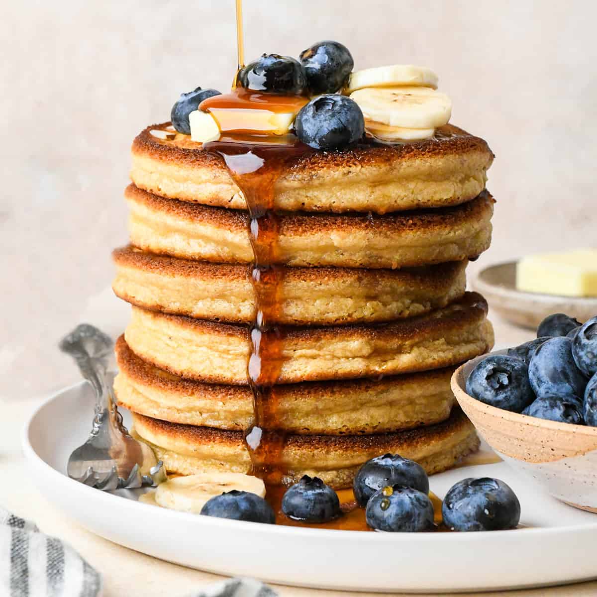 une pile de 6 crêpes à la farine d'amande avec du sirop, du beurre et des fruits