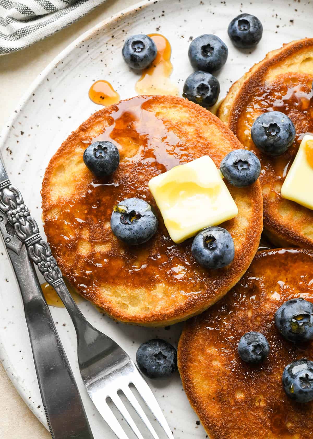 3 crêpes à la farine d'amande sur une assiette avec du beurre, des myrtilles et du sirop