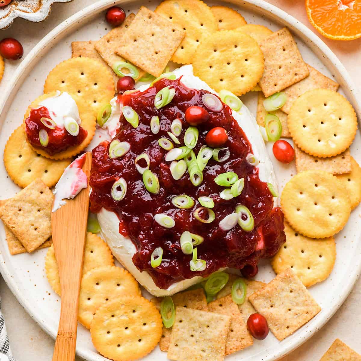 Cranberry Cream Cheese Dip surrounded by crackers with a knife that has spread some onto one cracker