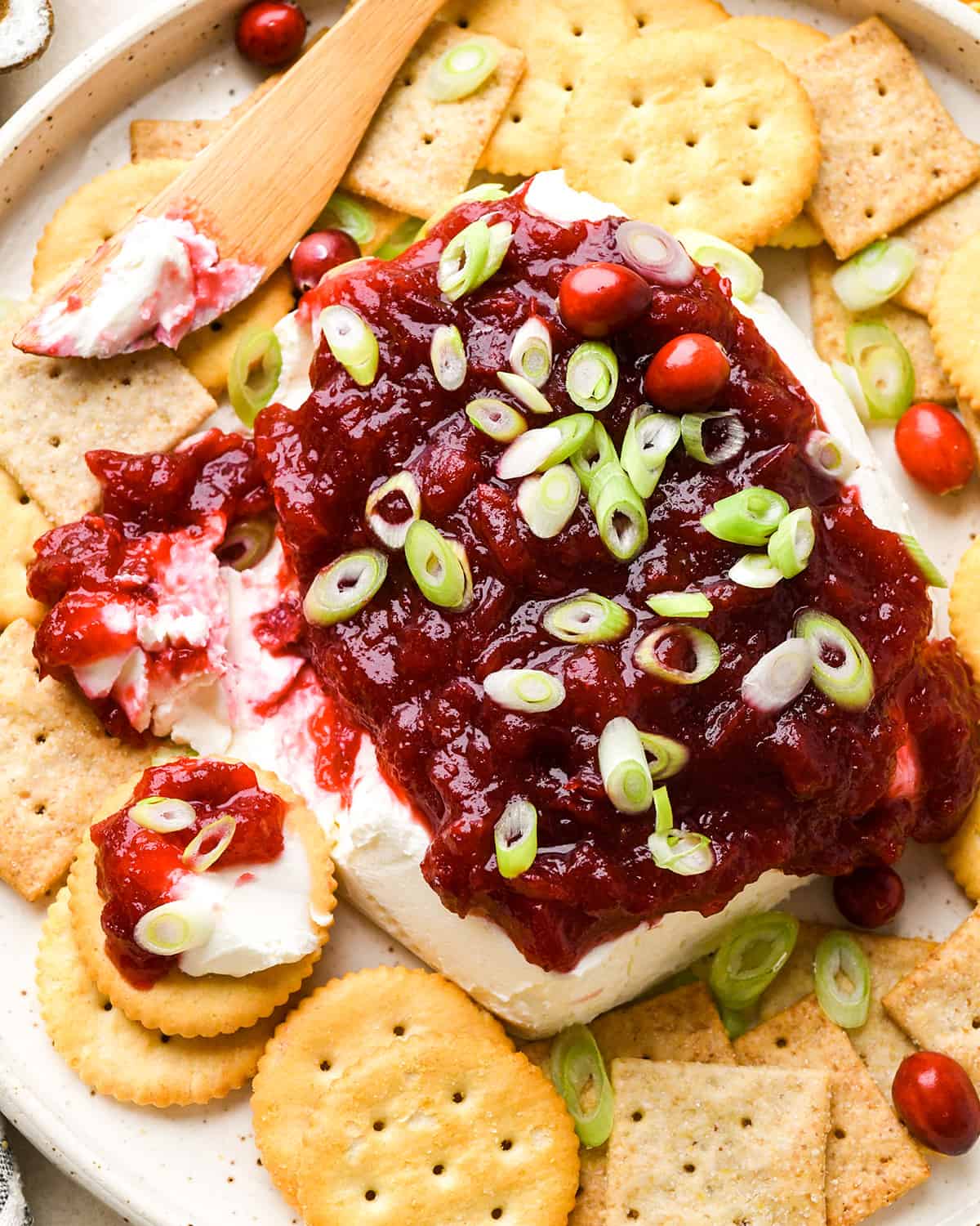 Cranberry Cream Cheese Dip surrounded by crackers with a knife that has spread some onto one cracker