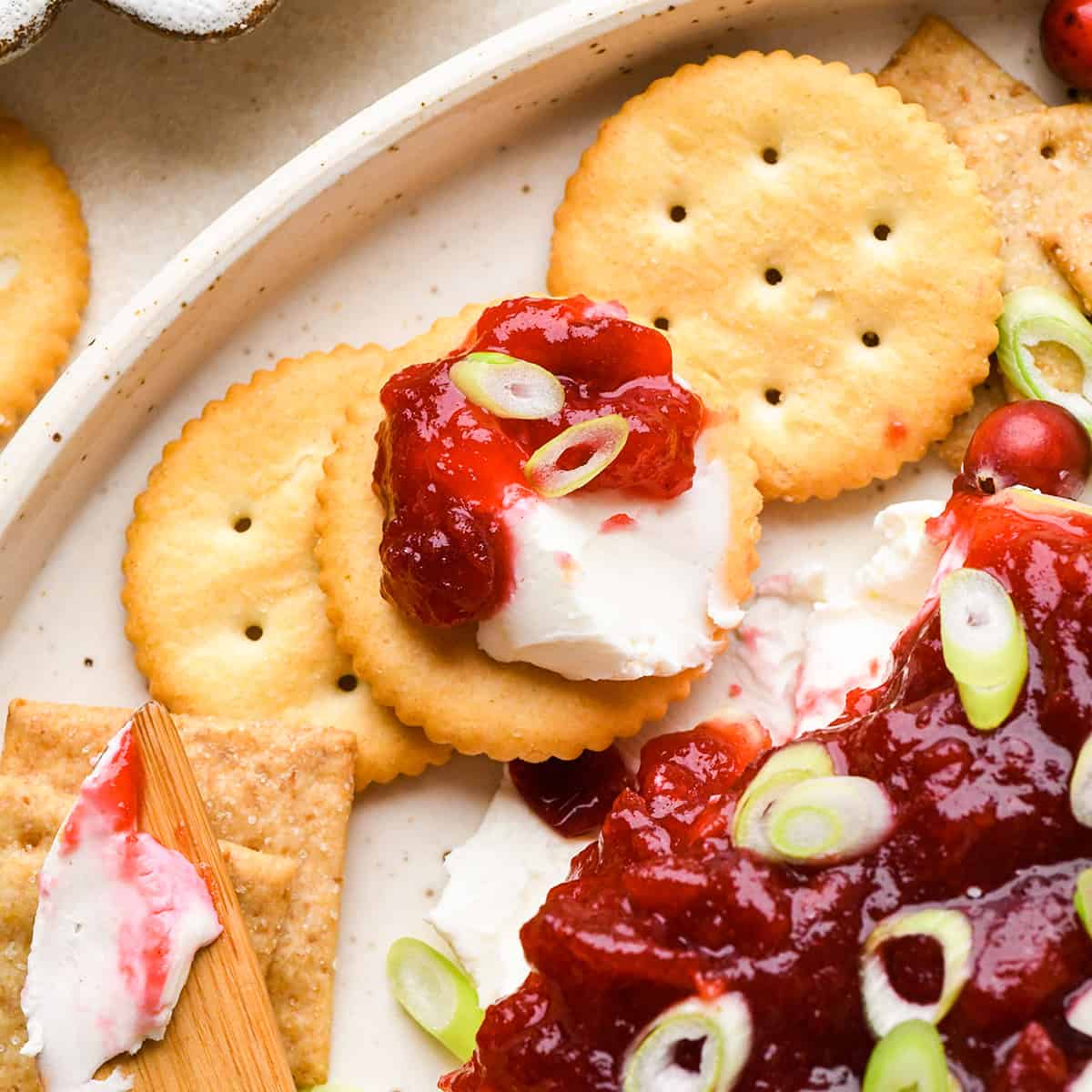 Cranberry Cream Cheese Dip spread onto a cracker next to the rest of the dip