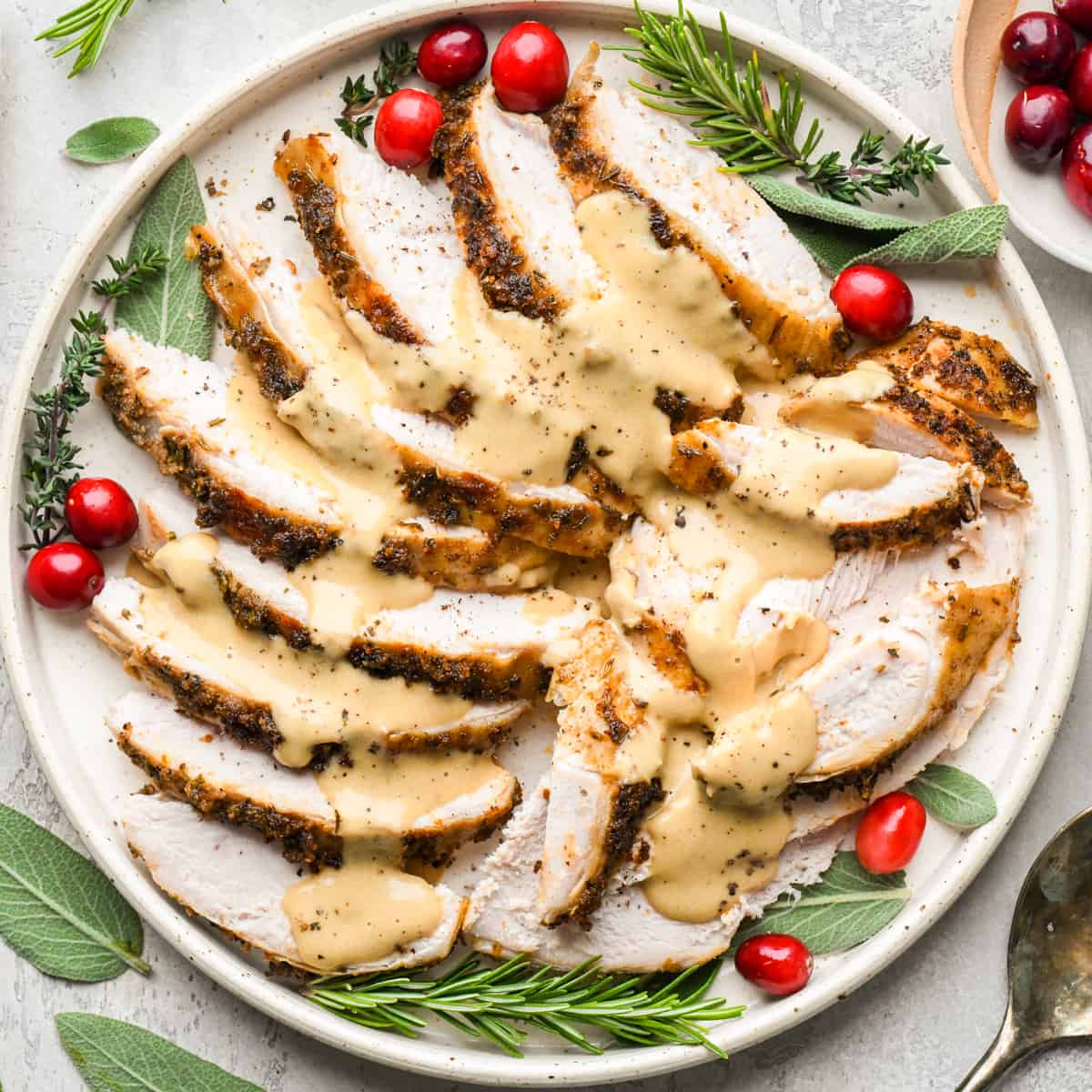 Crock Pot Turkey Breast sliced into pieces on a plate with gravy, herbs and cranberries