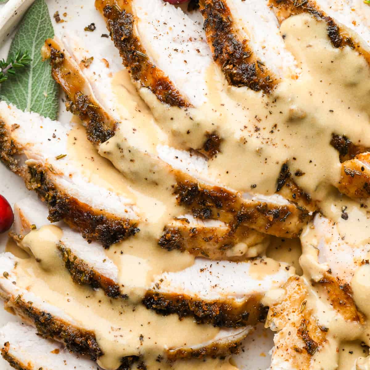 up close photo of Crock Pot Turkey Breast sliced into pieces on a plate with gravy, herbs and cranberries