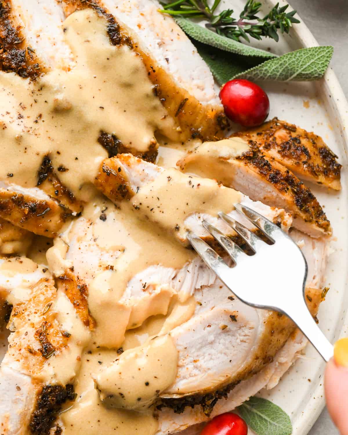 a fork taking a piece of Crock Pot Turkey Breast on a plate with gravy, herbs and cranberries