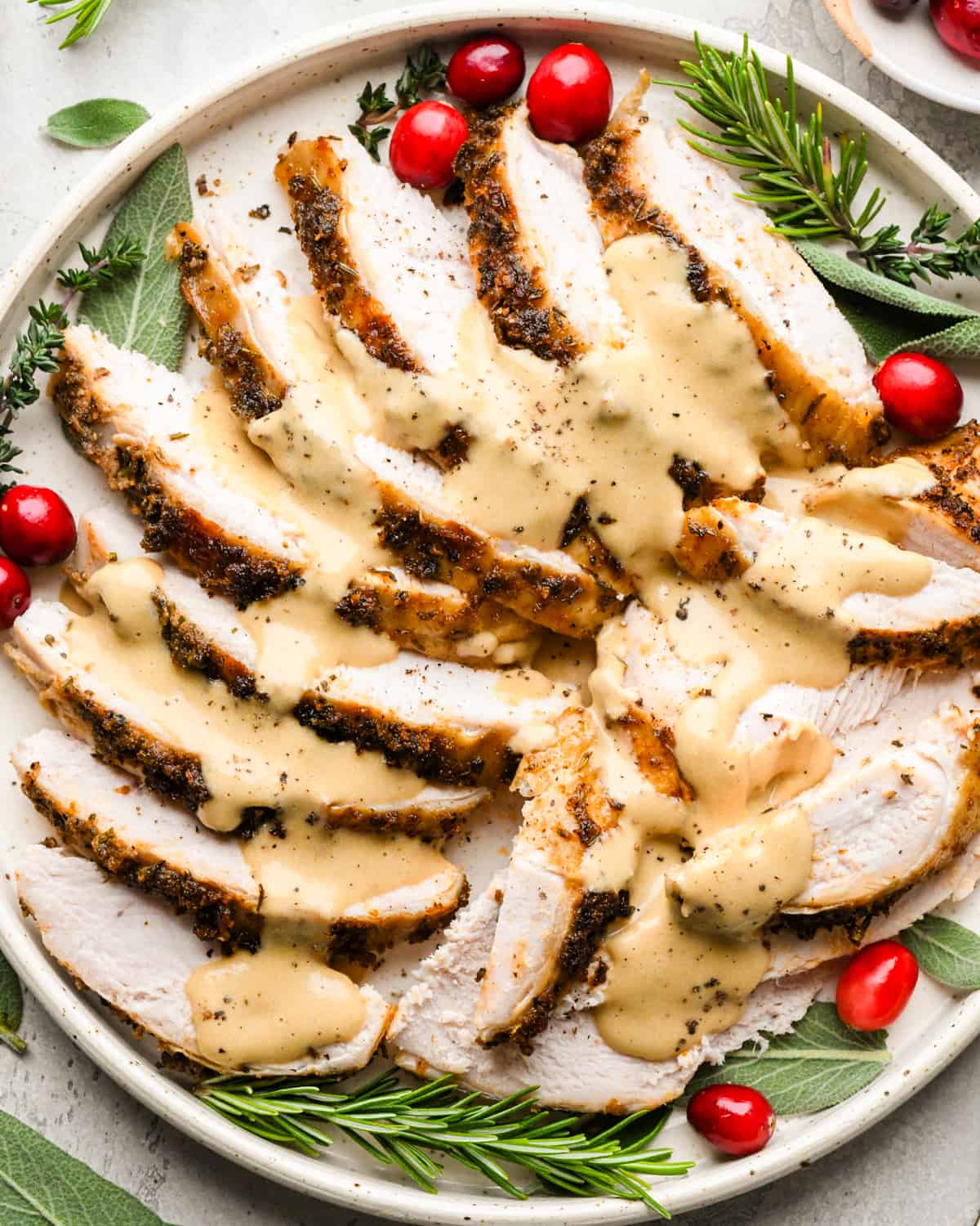 Crock Pot Turkey Breast sliced into pieces on a plate with gravy, herbs and cranberries