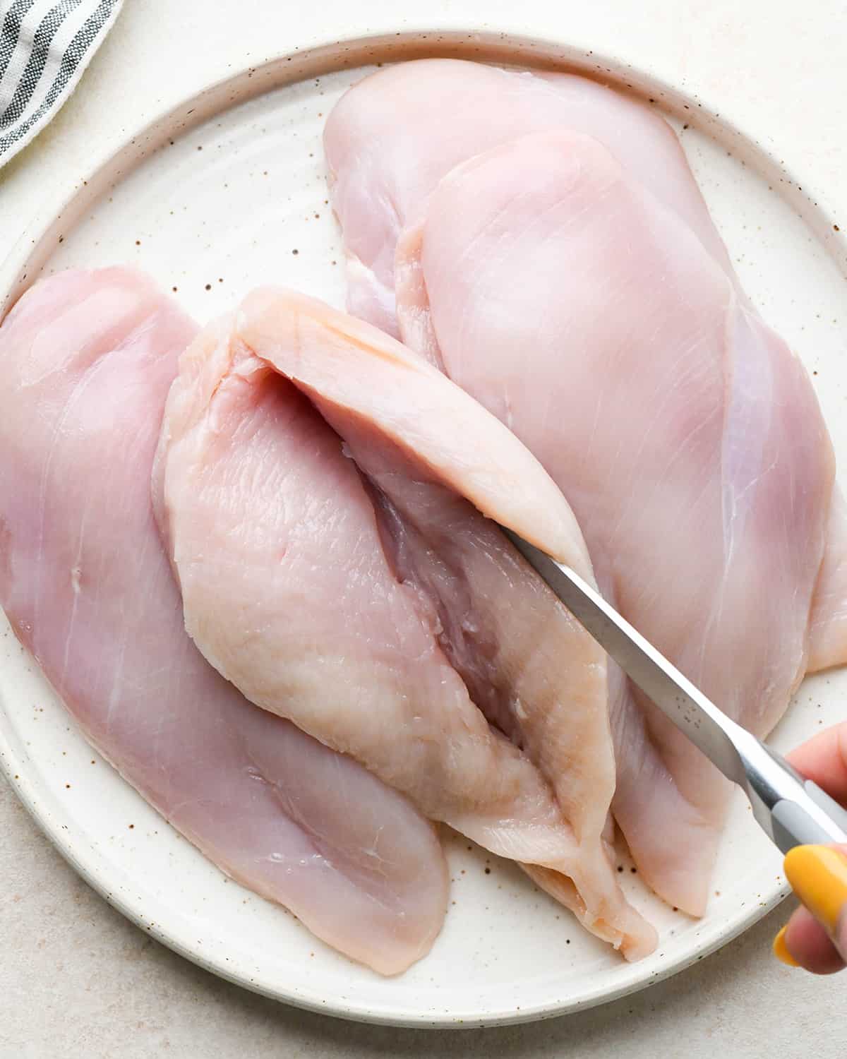 a knife cutting a slit into a chicken breast