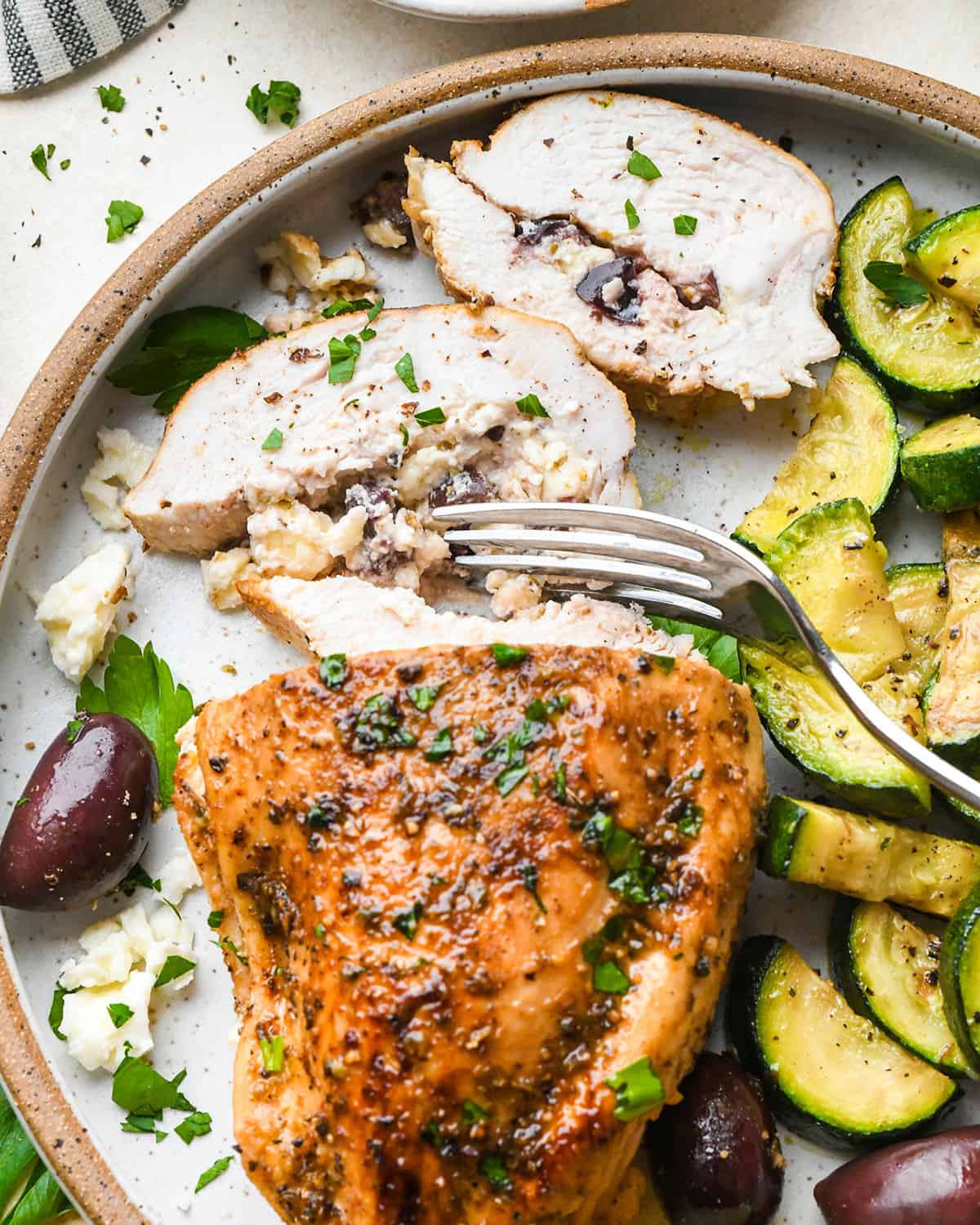 a greek stuffed chicken breast with 2 slices cut out of it and a fork taking a bite