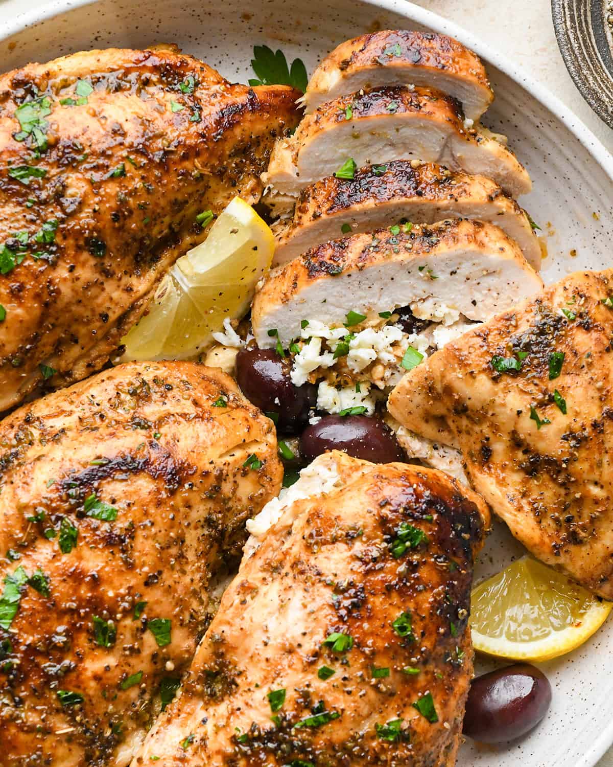 4 Feta Stuffed Chicken Breasts on a plate, one with 4 slices cut out of it so the inside is visible 