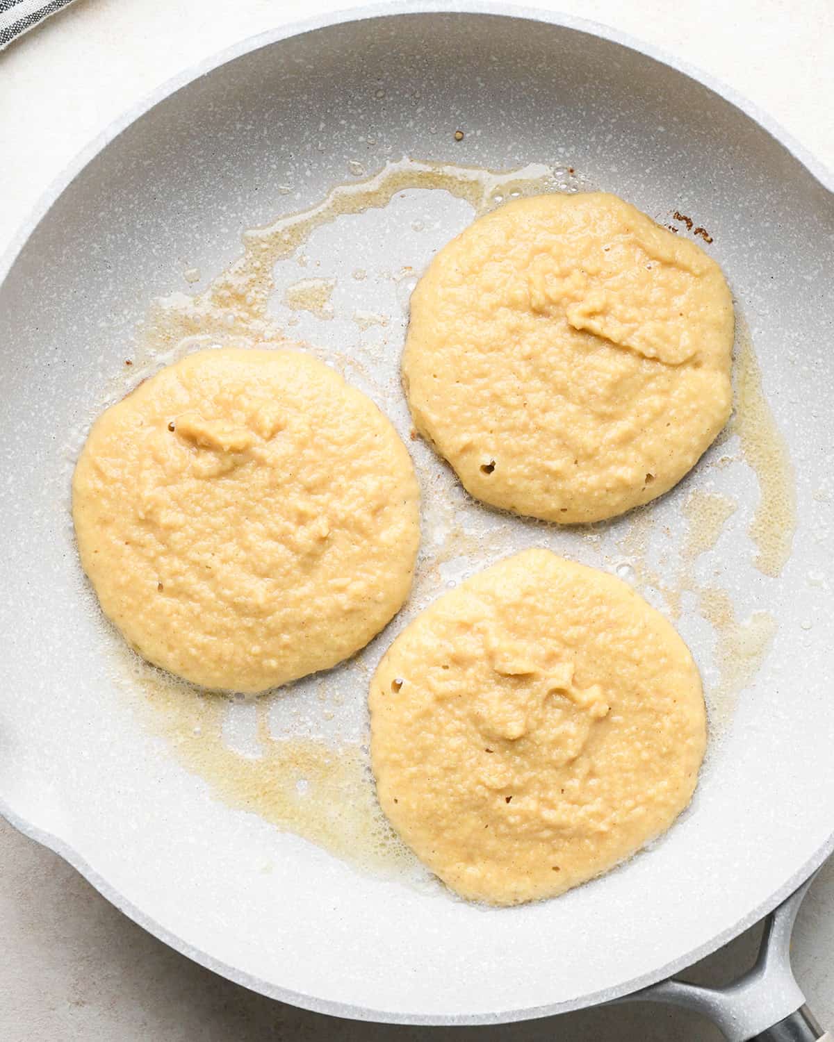 3 almond flour pancakes cooking in a pan on the first side