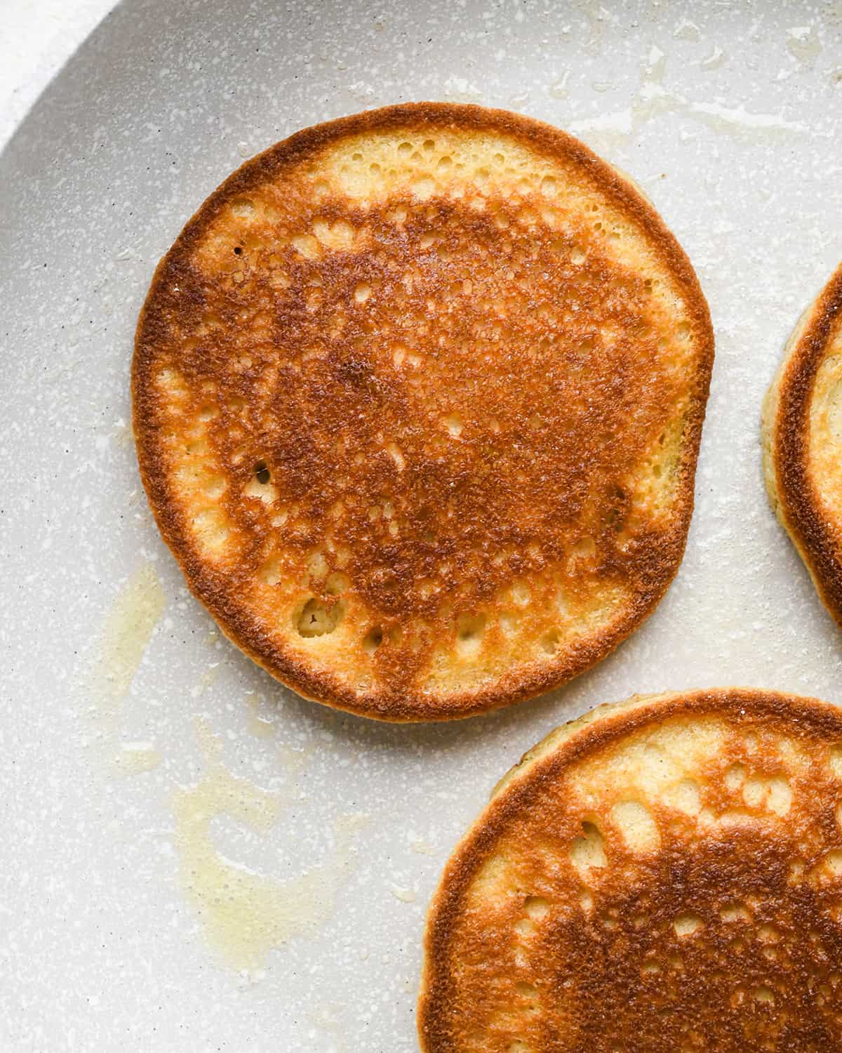 3 almond flour pancakes cooking on a pan on the second side