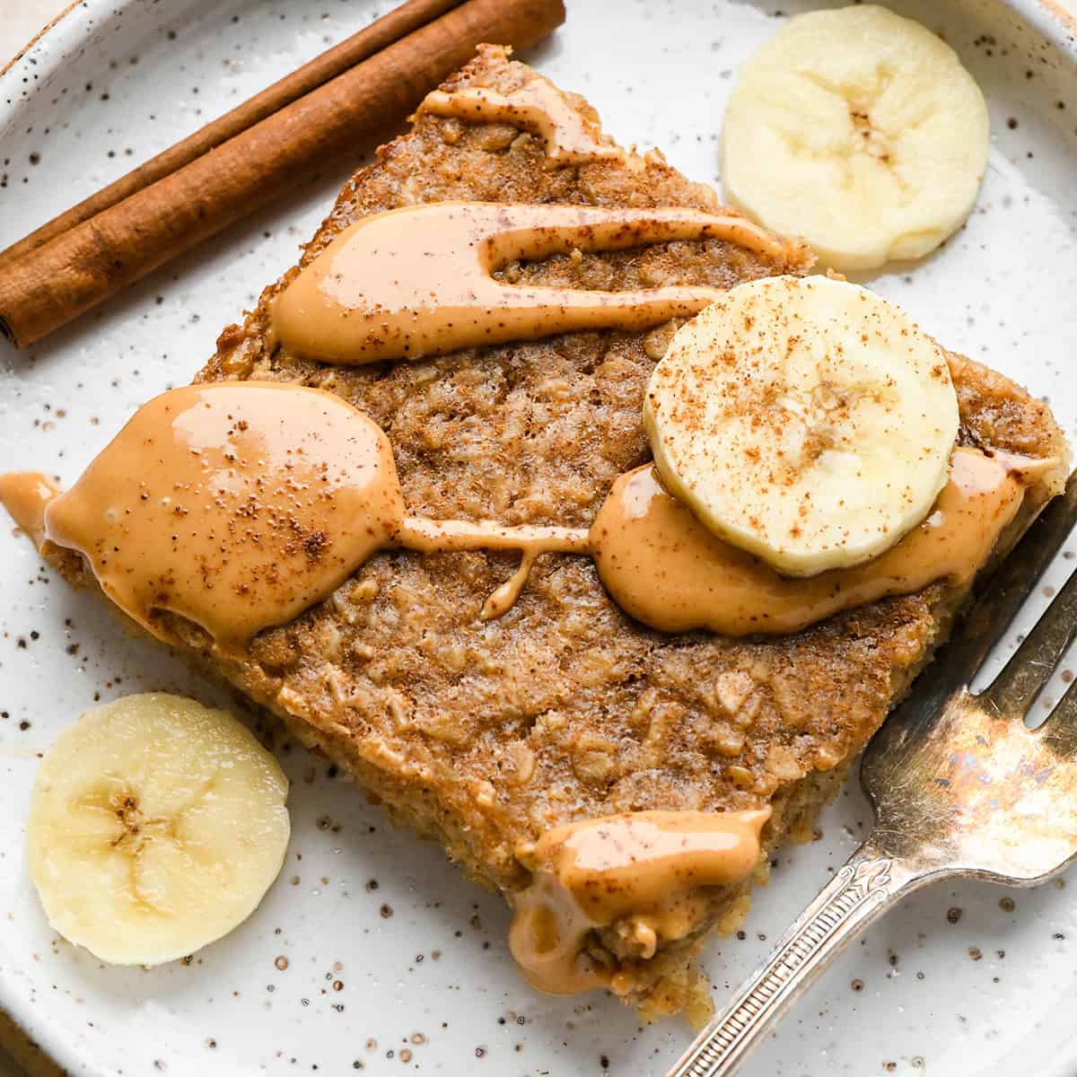 a slice of Peanut Butter Banana Baked Oatmeal on a plate with a drizzle of peanut butter and sliced bananas