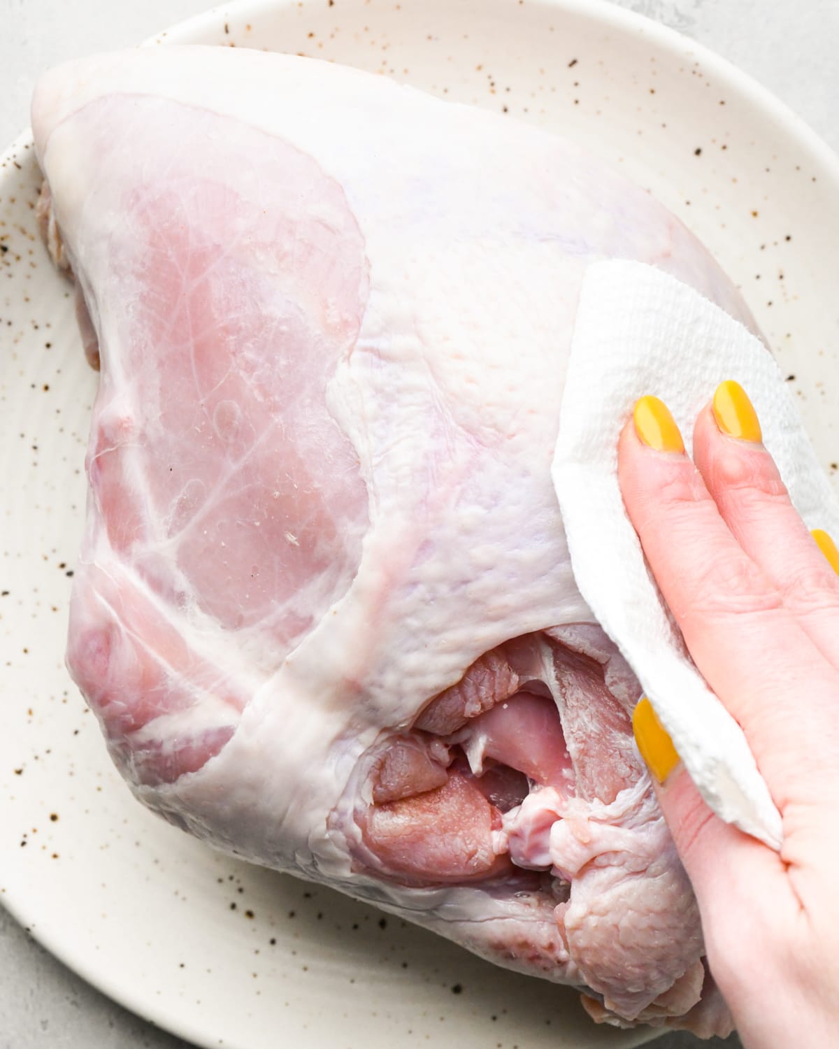 a hand holding a paper towel patting a turkey breast dry