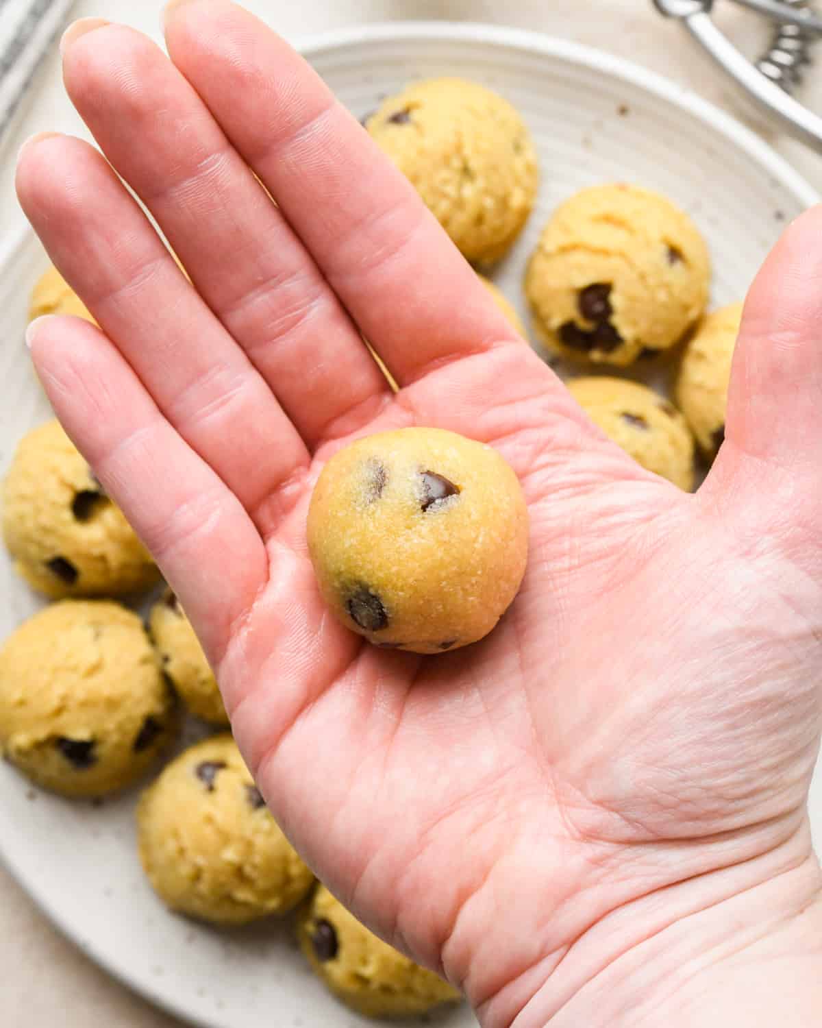 a hand rolling an almond flour chocolate chip cookie into a ball