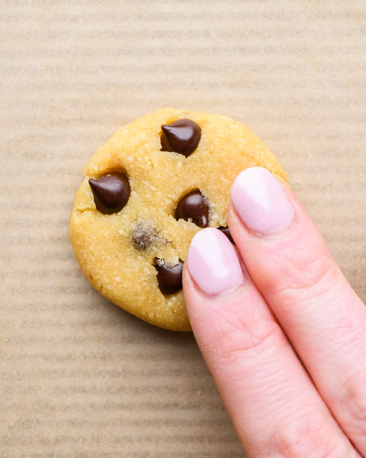 a hand pressing down an almond flour cookie dough ball