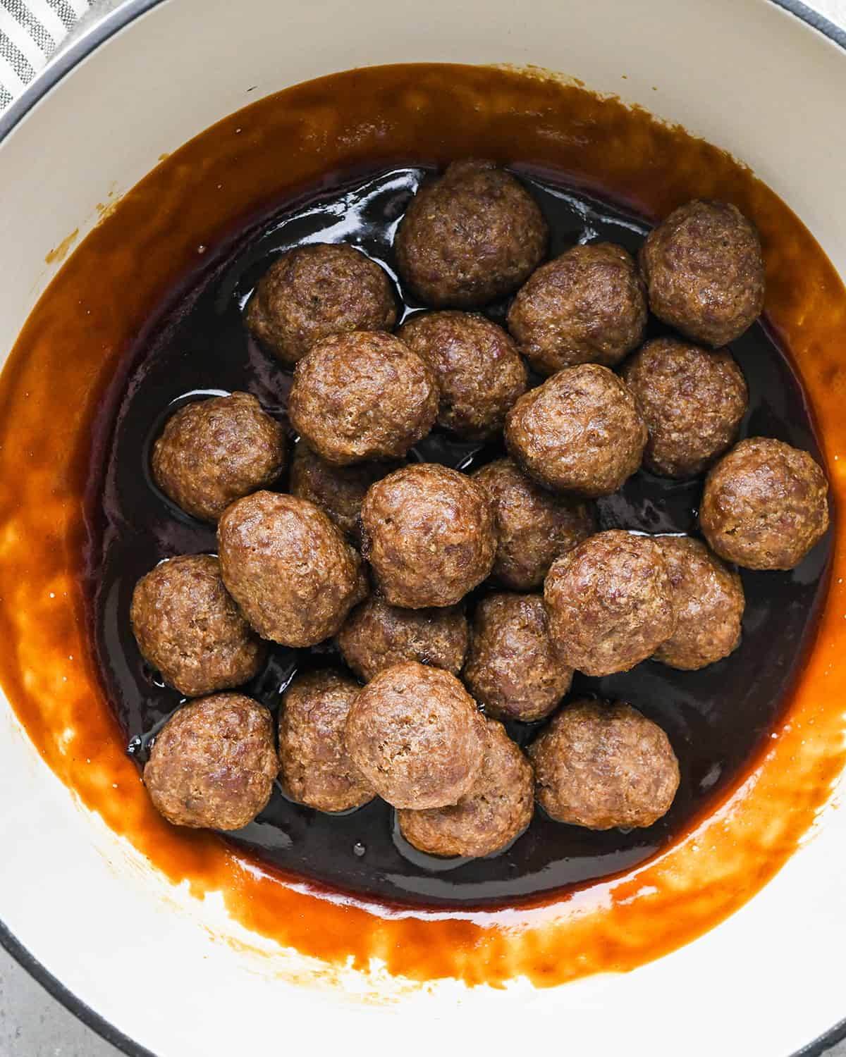 Asian Meatballs being added to the sauce in a pot before mixing