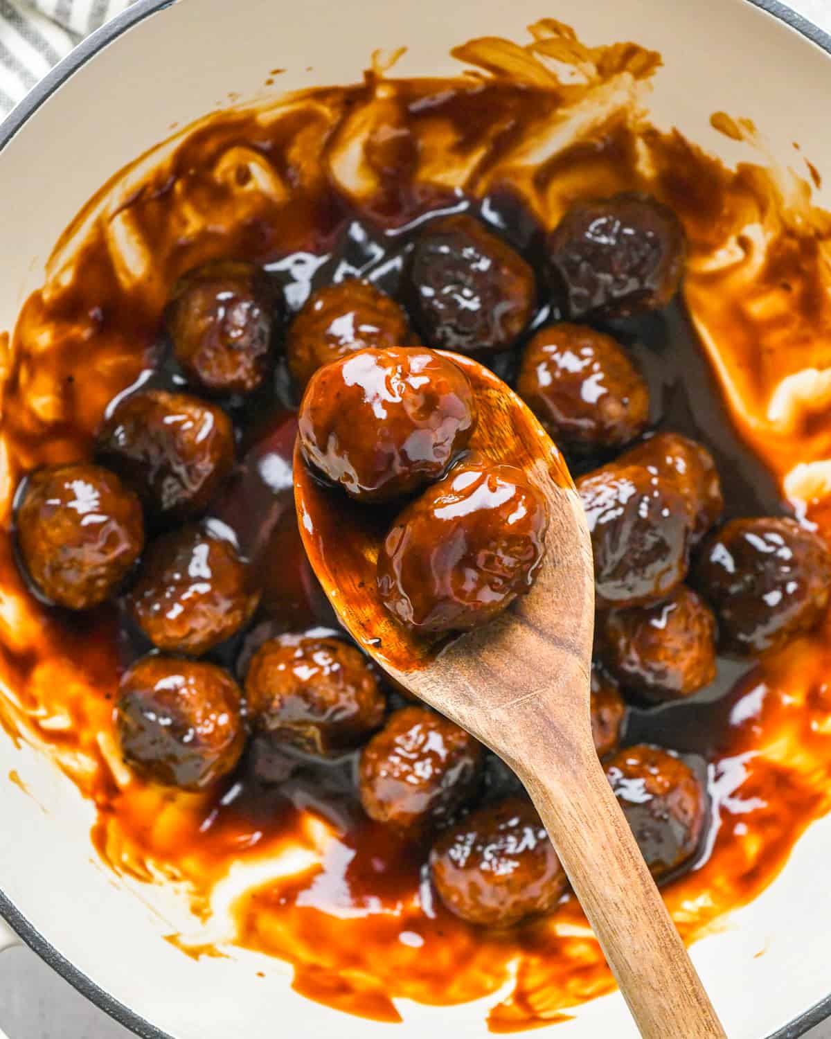 Asian Meatballs mixed with sauce in a pot with a wooden spoon