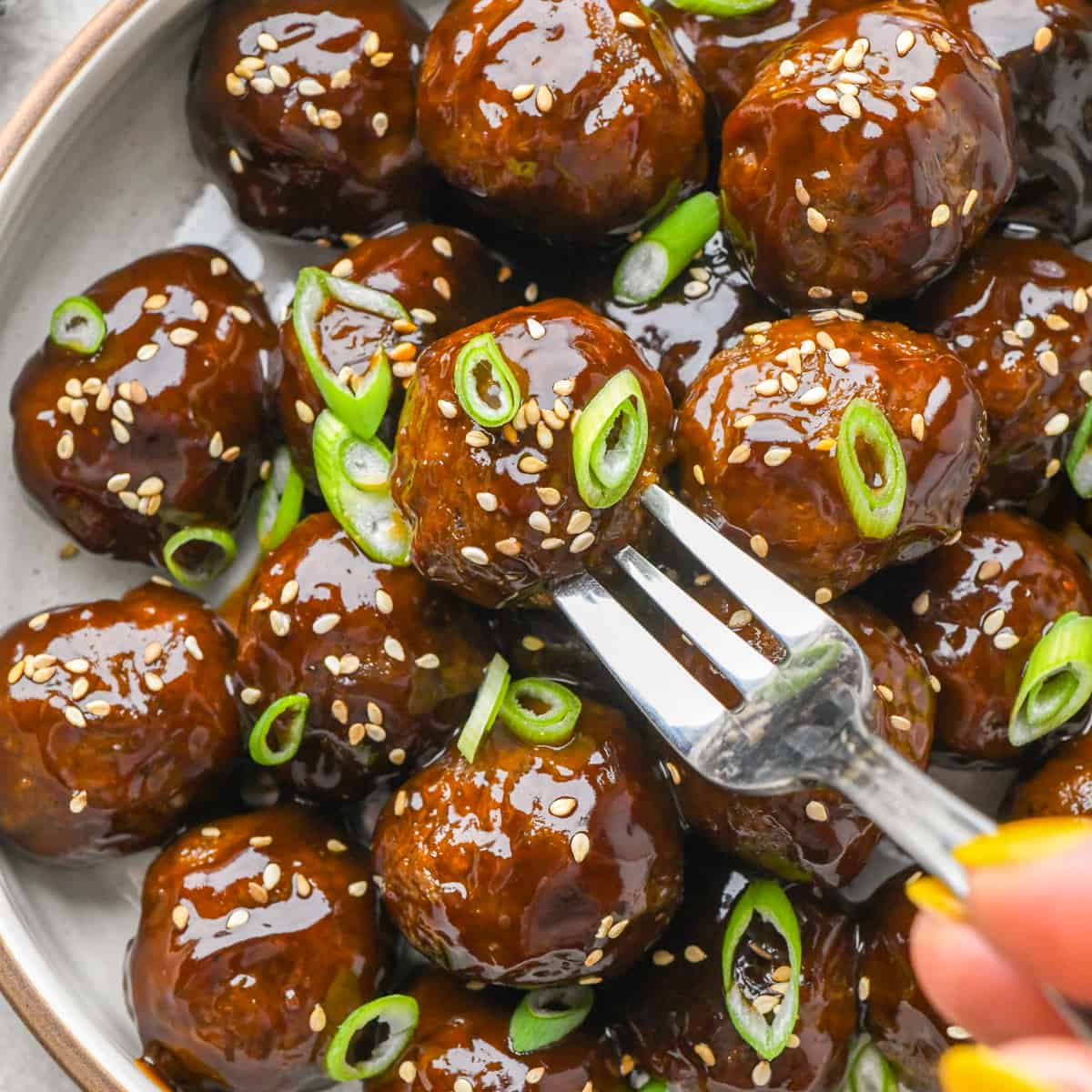 Asian Meatballs garnished with sesame seeds and green onions on a plate with a fork