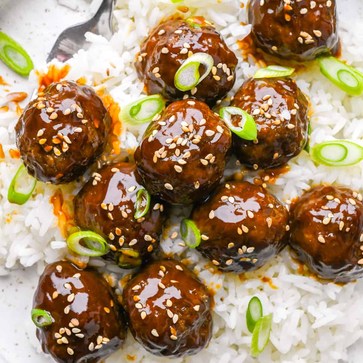 9 Asian Meatballs on top of rice on a plate garnished with sesame seeds and green onions 