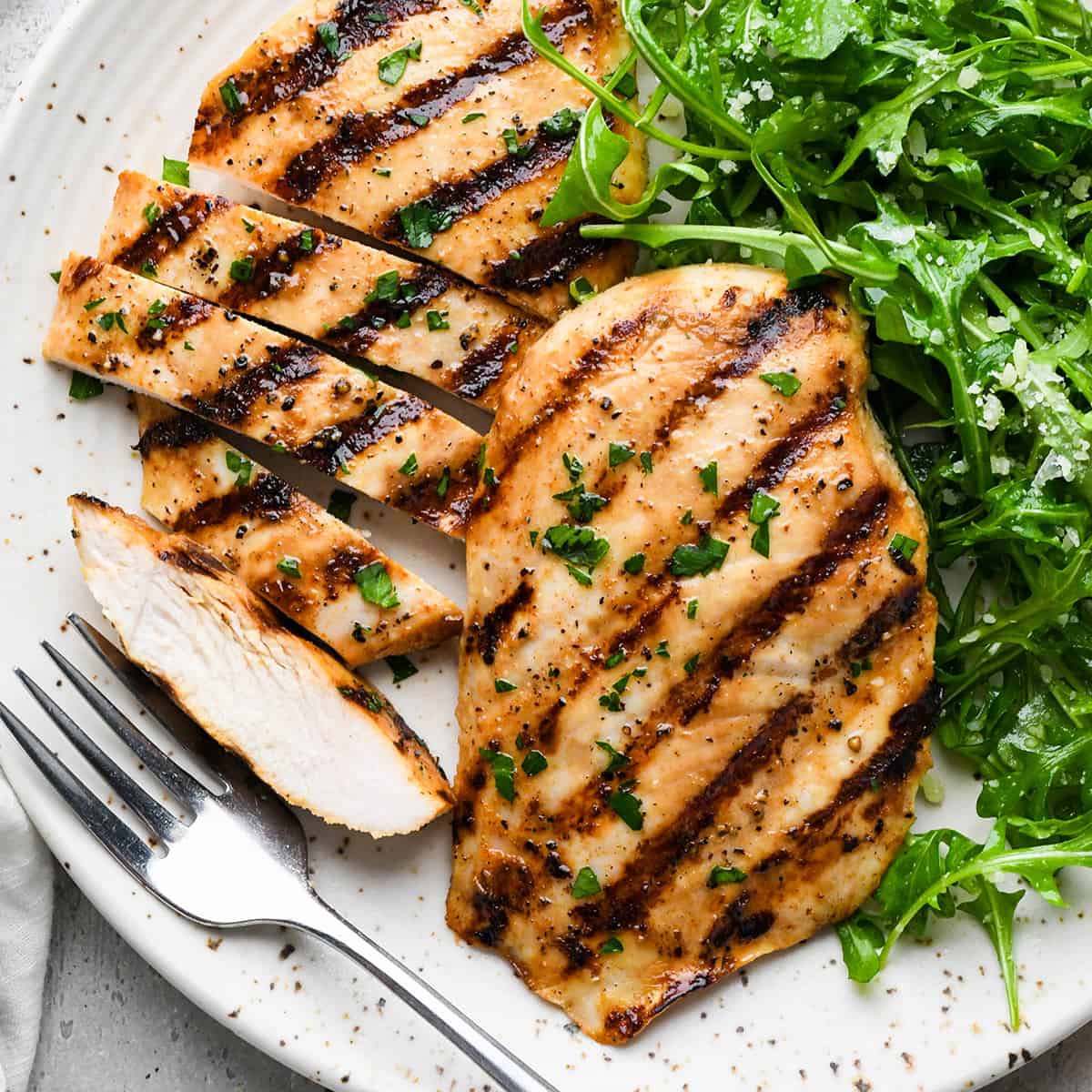 two Buttermilk Chicken breasts on a plate, one cut into strips, with a fork and salad