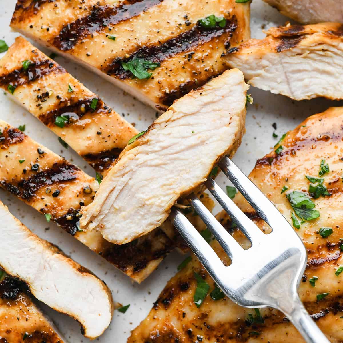 sliced grilled buttermilk chicken, one piece on a fork, garnished with herbs