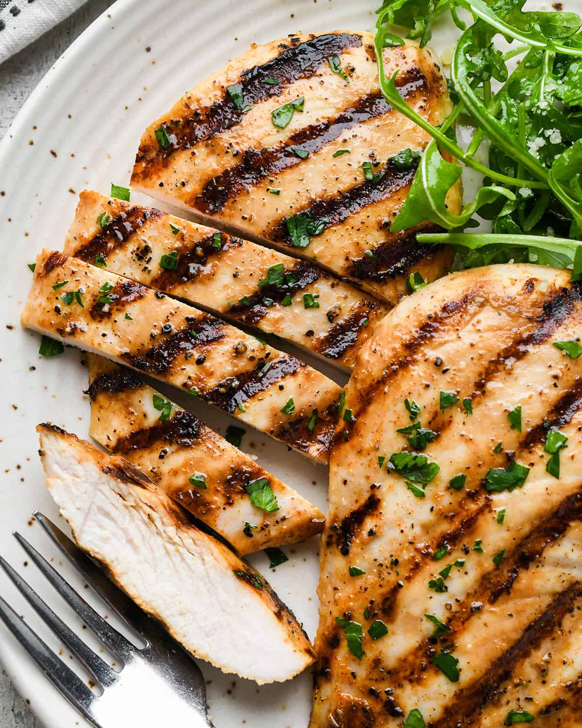 two buttermilk chicken breasts on a plate, one sliced into strips