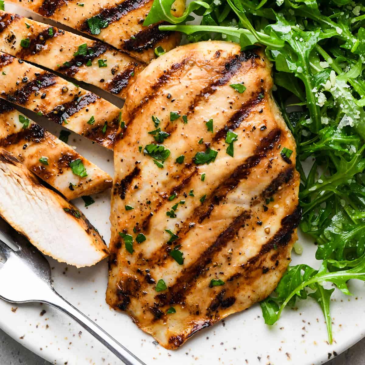 two buttermilk chicken breasts on a plate, one sliced into strips