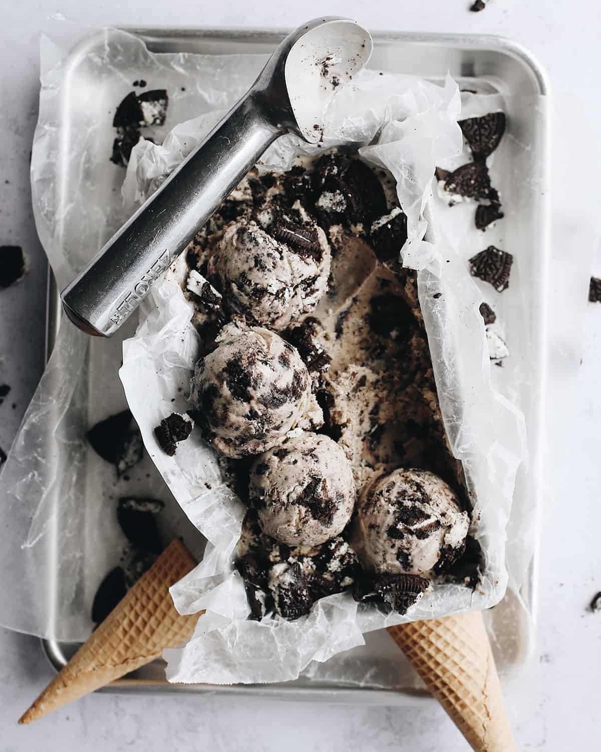 Cookies and Cream Ice Cream in a container with an ice cream scoop and cone