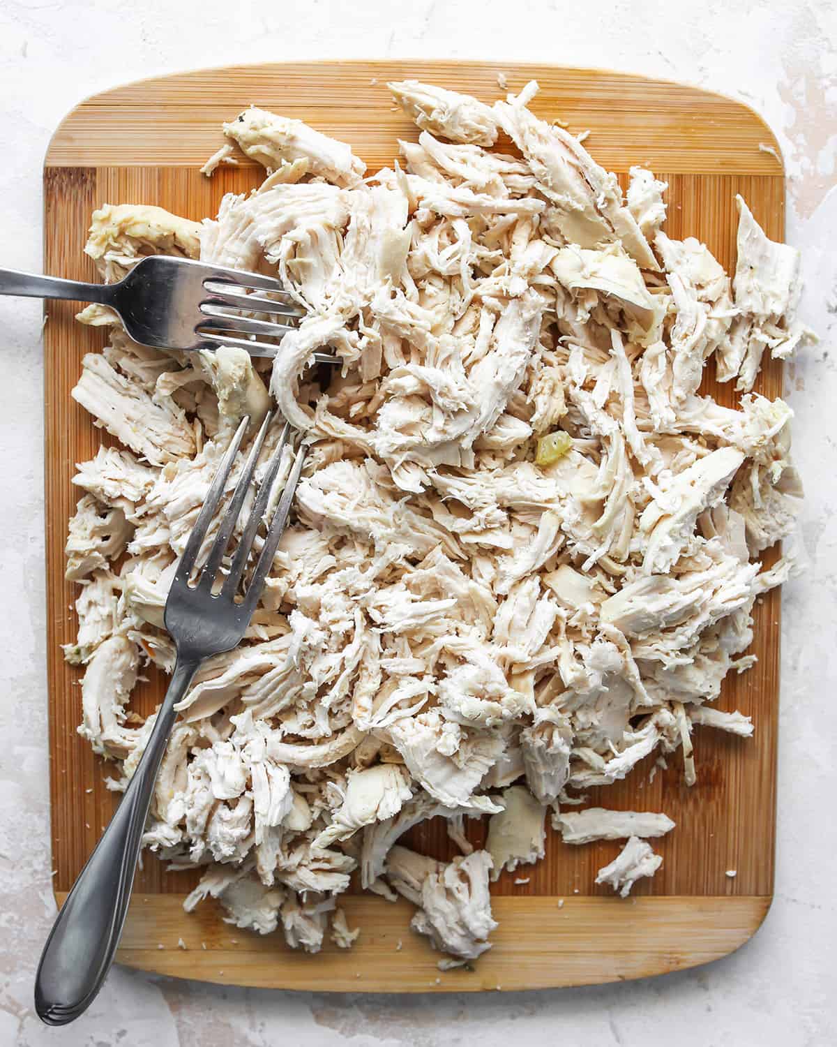 shredded chicken on a cutting board with two forks