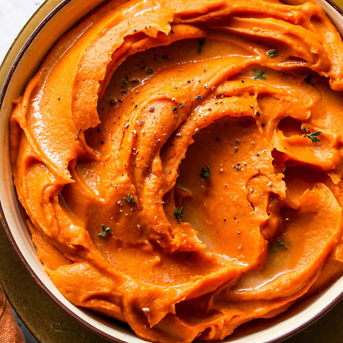 Mashed Sweet Potatoes in a bowl garnished with melted butter and chopped thyme