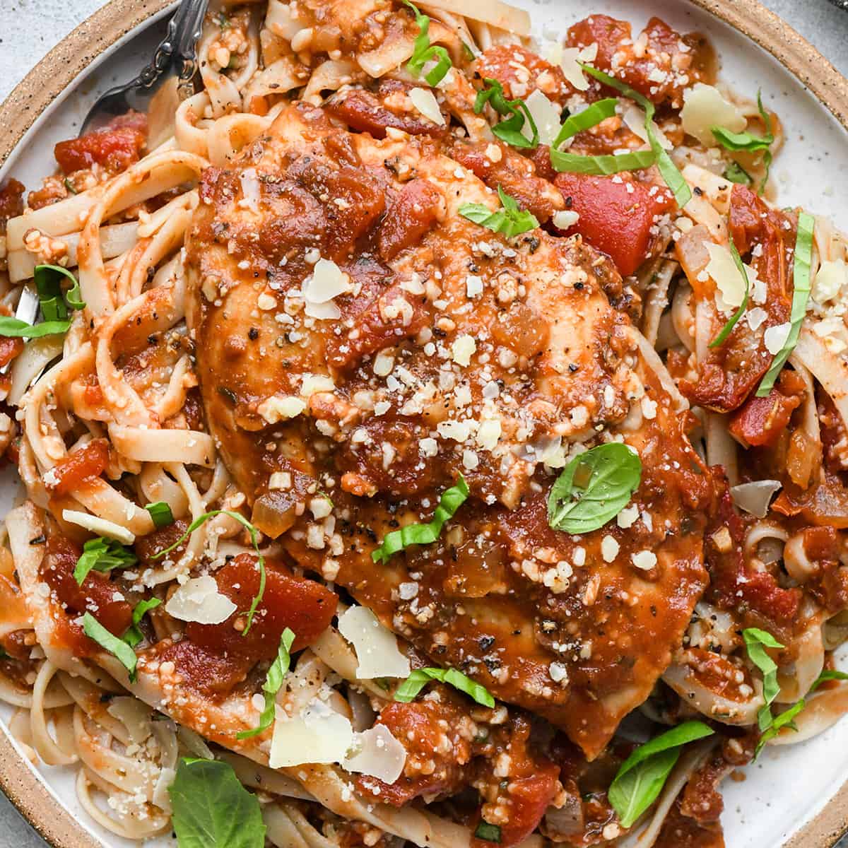 Slow Cooker Italian Chicken breast on top of pasta on a plate garnished with basil and parmesan cheese