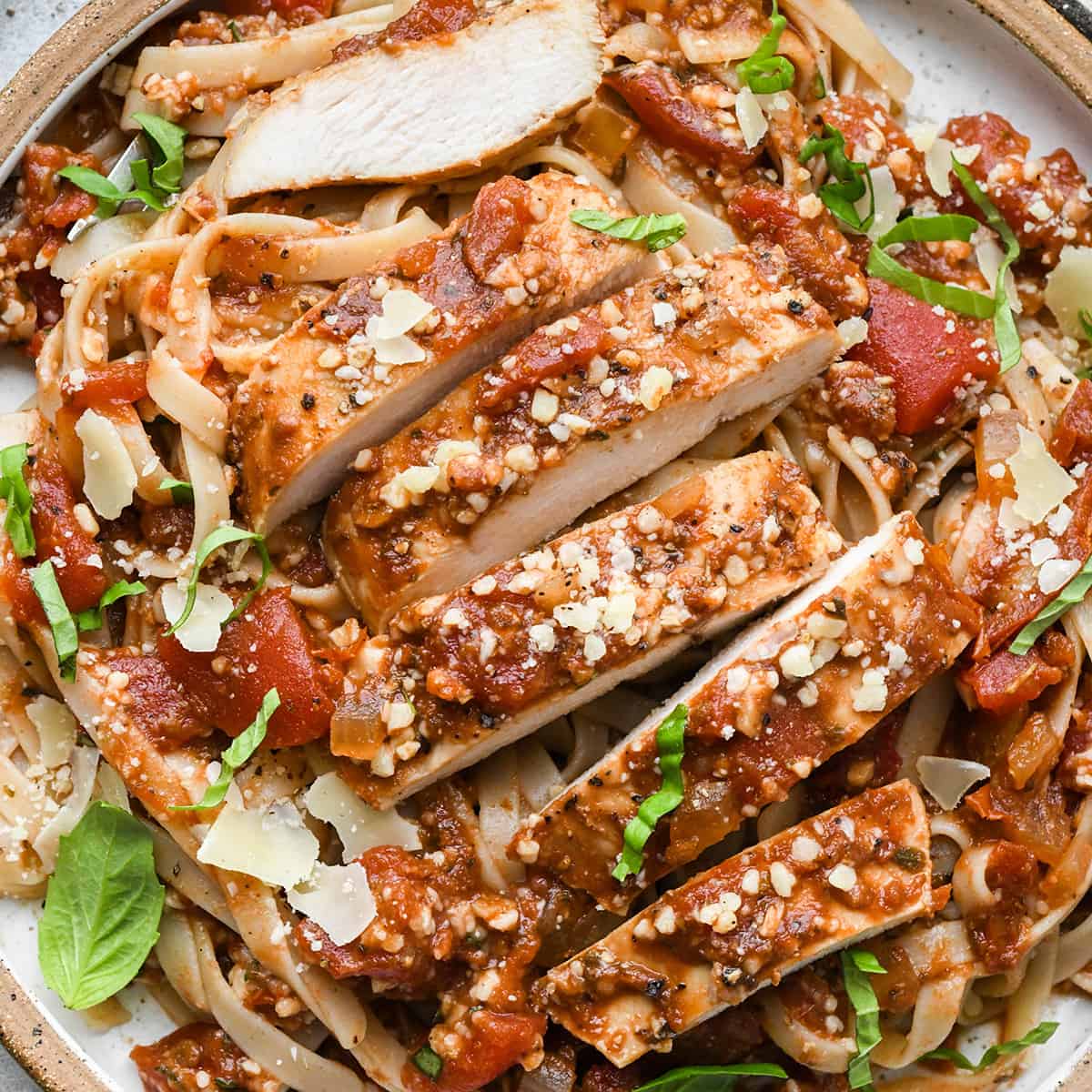 Slow Cooker Italian Chicken breast cut into strips on top of pasta on a plate garnished with basil and parmesan cheese