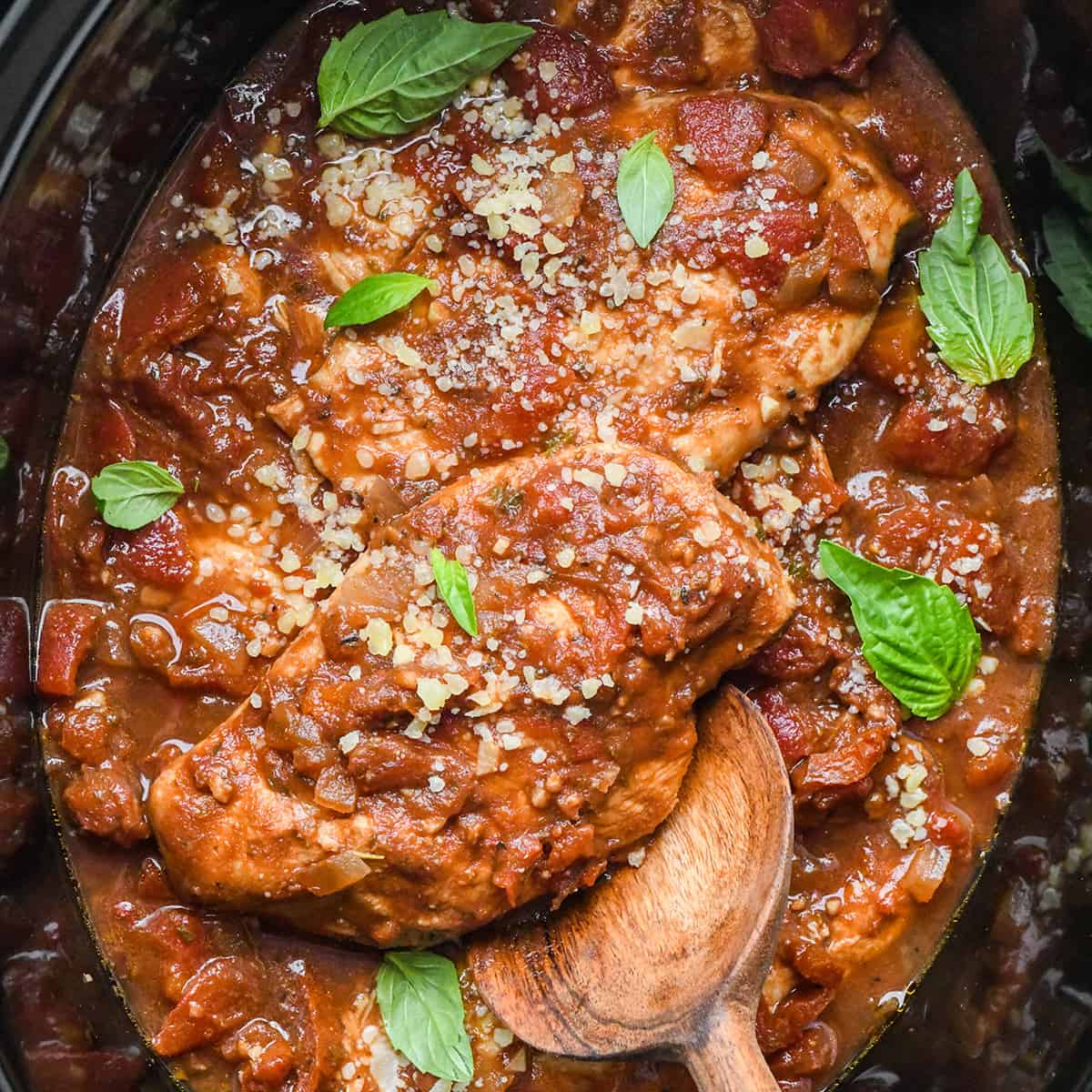 Deux poitrines de poulet italien à la mijoteuse dans un plat, garnies de basilic et de fromage parmesan