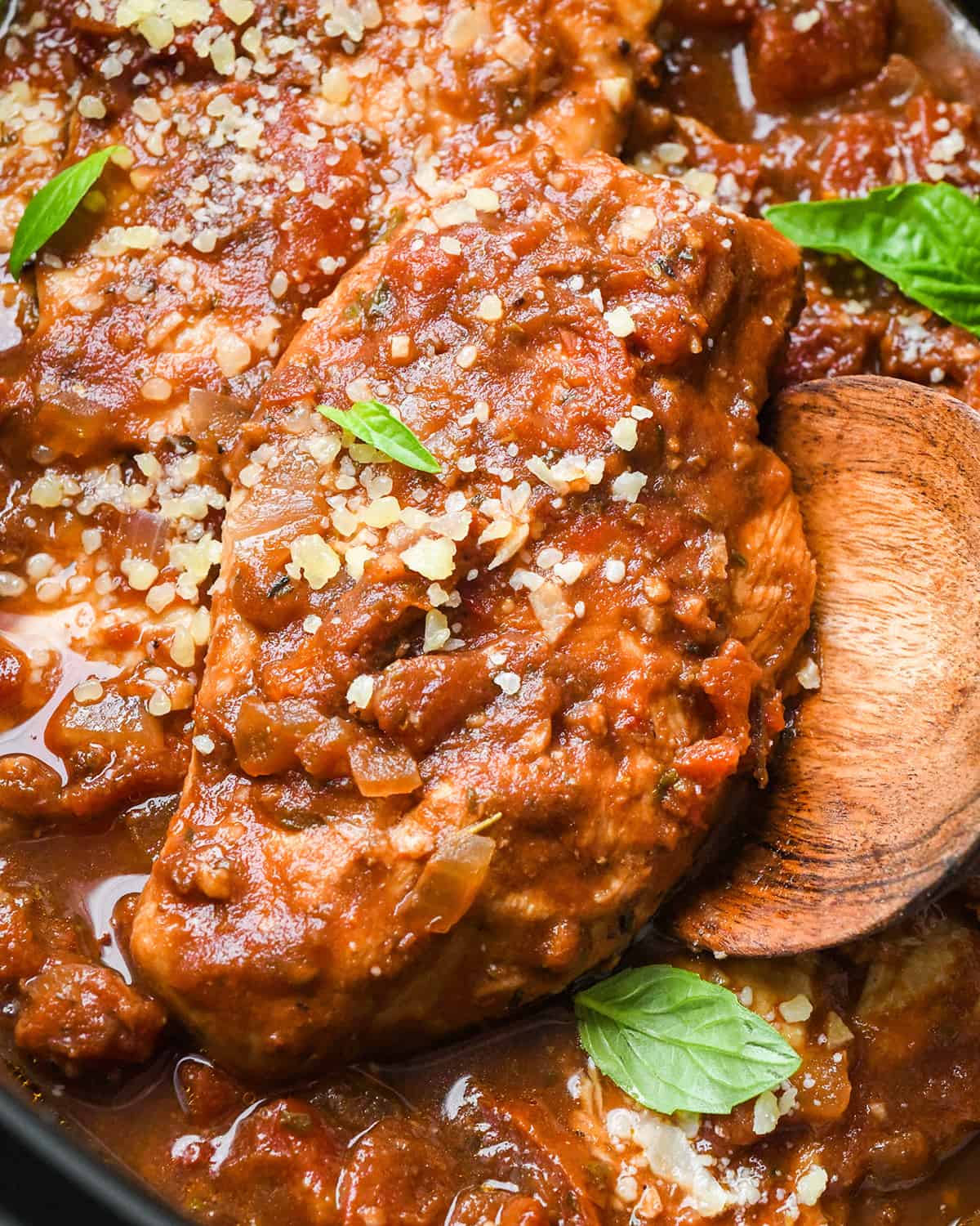 a wooding spoon under a Slow Cooker Italian Chicken breast in the crockpot garnished with basil and parmesan cheese