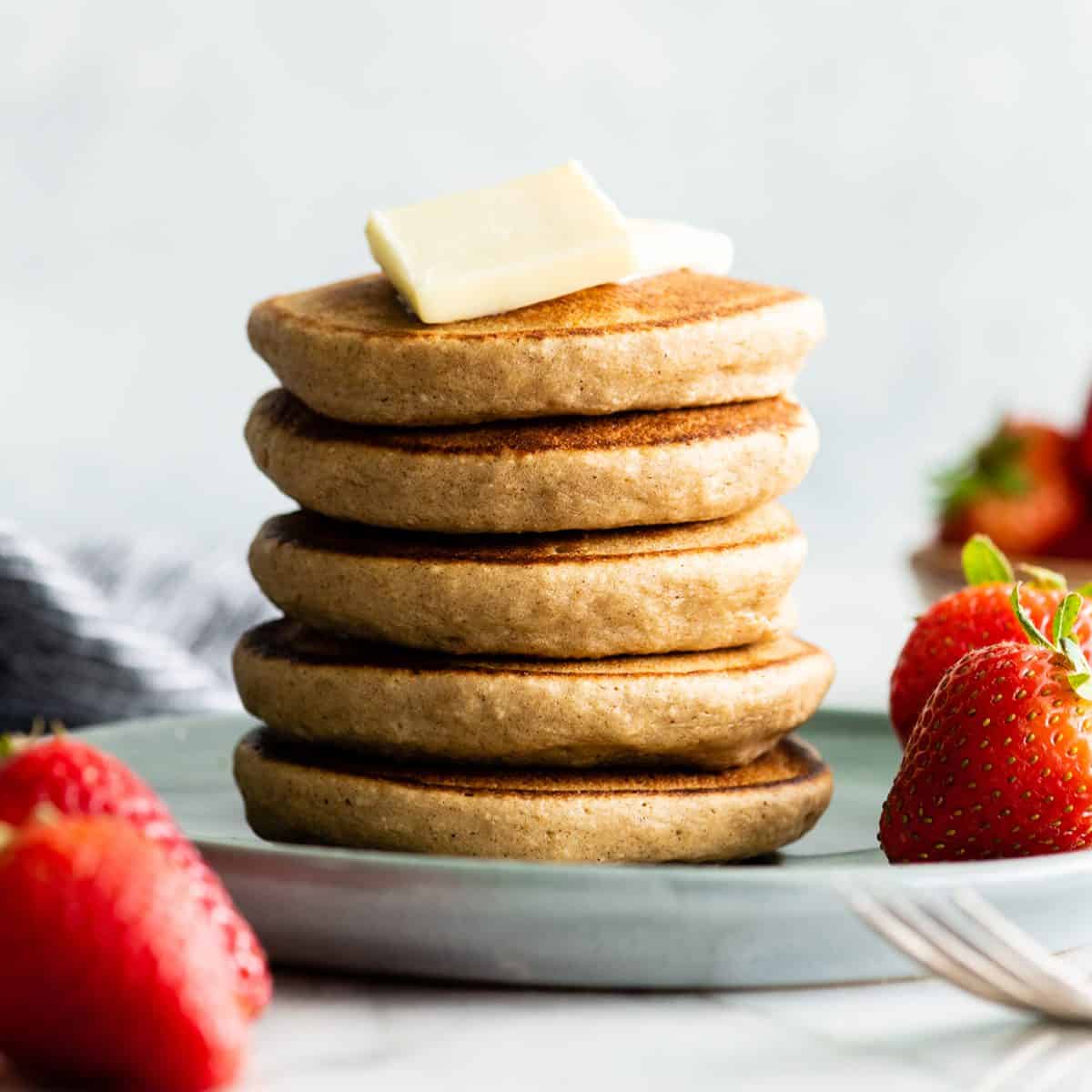 a stack of 5 banana oatmeal pancakes with butter on top and strawberries on the side