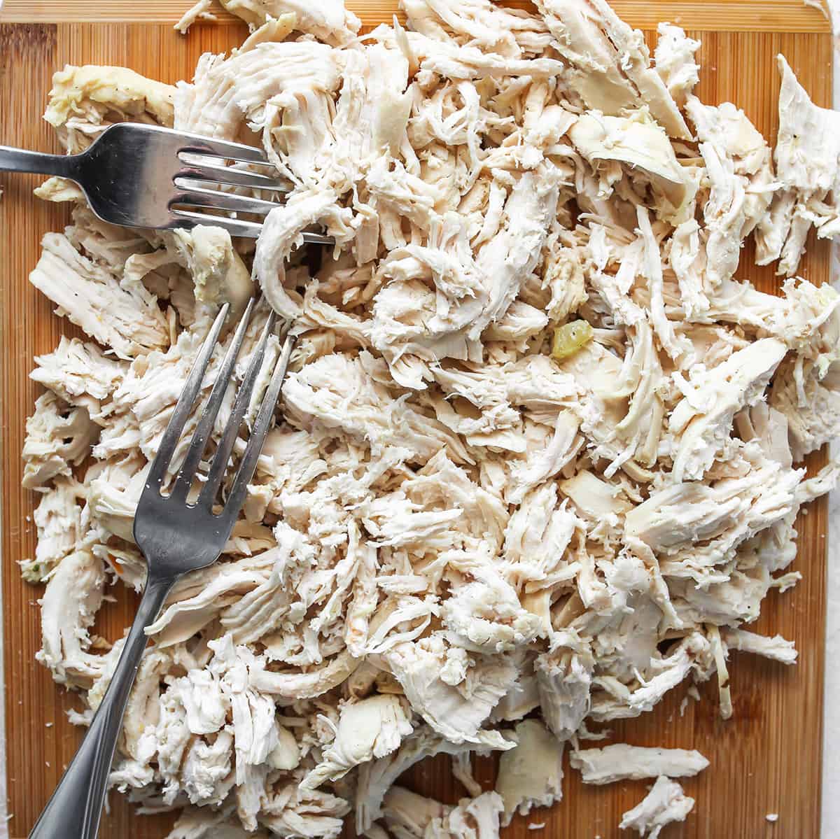 cooked, shredded chicken on a cutting board with 2 forks