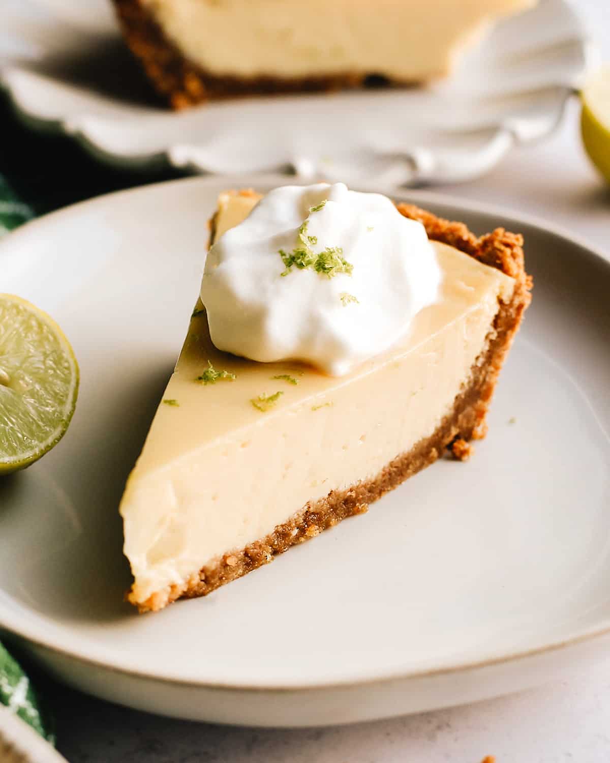a slice of key lime pie on a plate topped with whipped cream and lime zest 