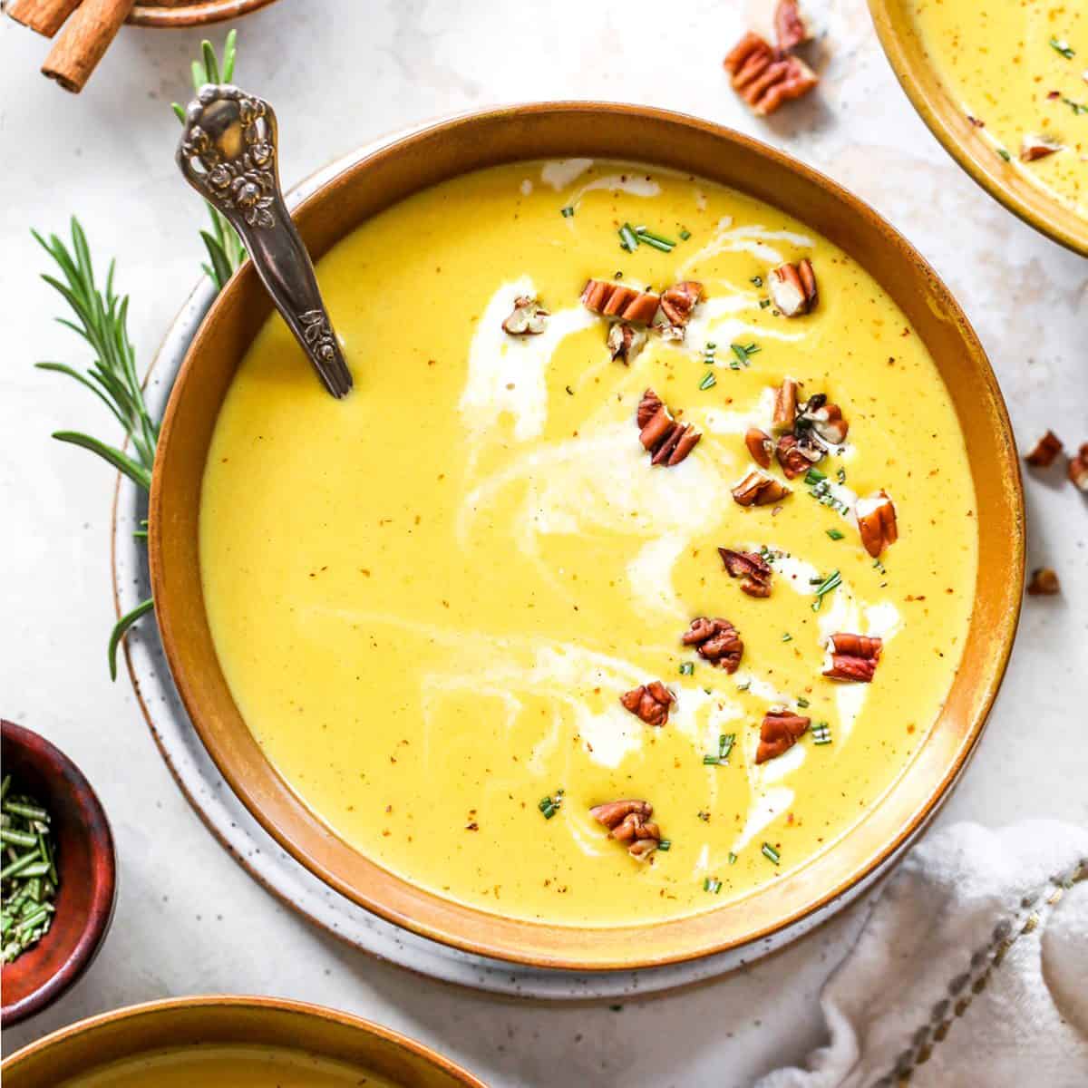 a bowl of butternut squash soup garnished with pecans, cream and rosemary