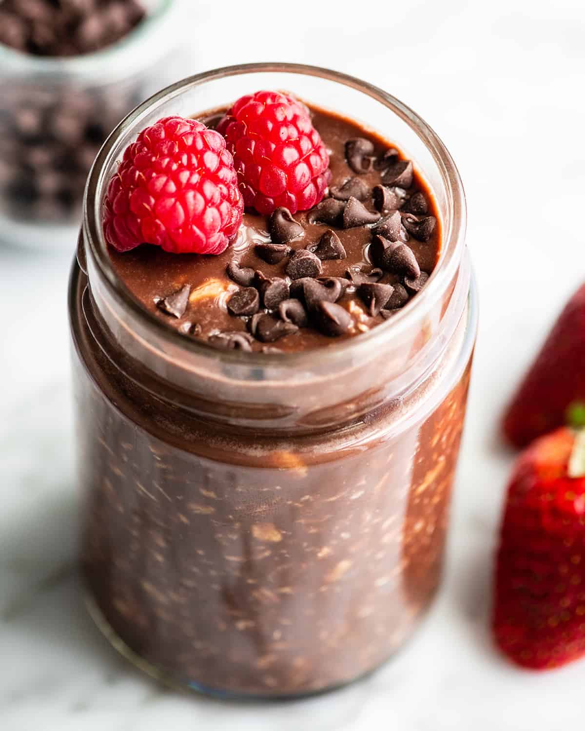 a jar of chocolate overnight oats topped with mini chocolate chips and two raspberries