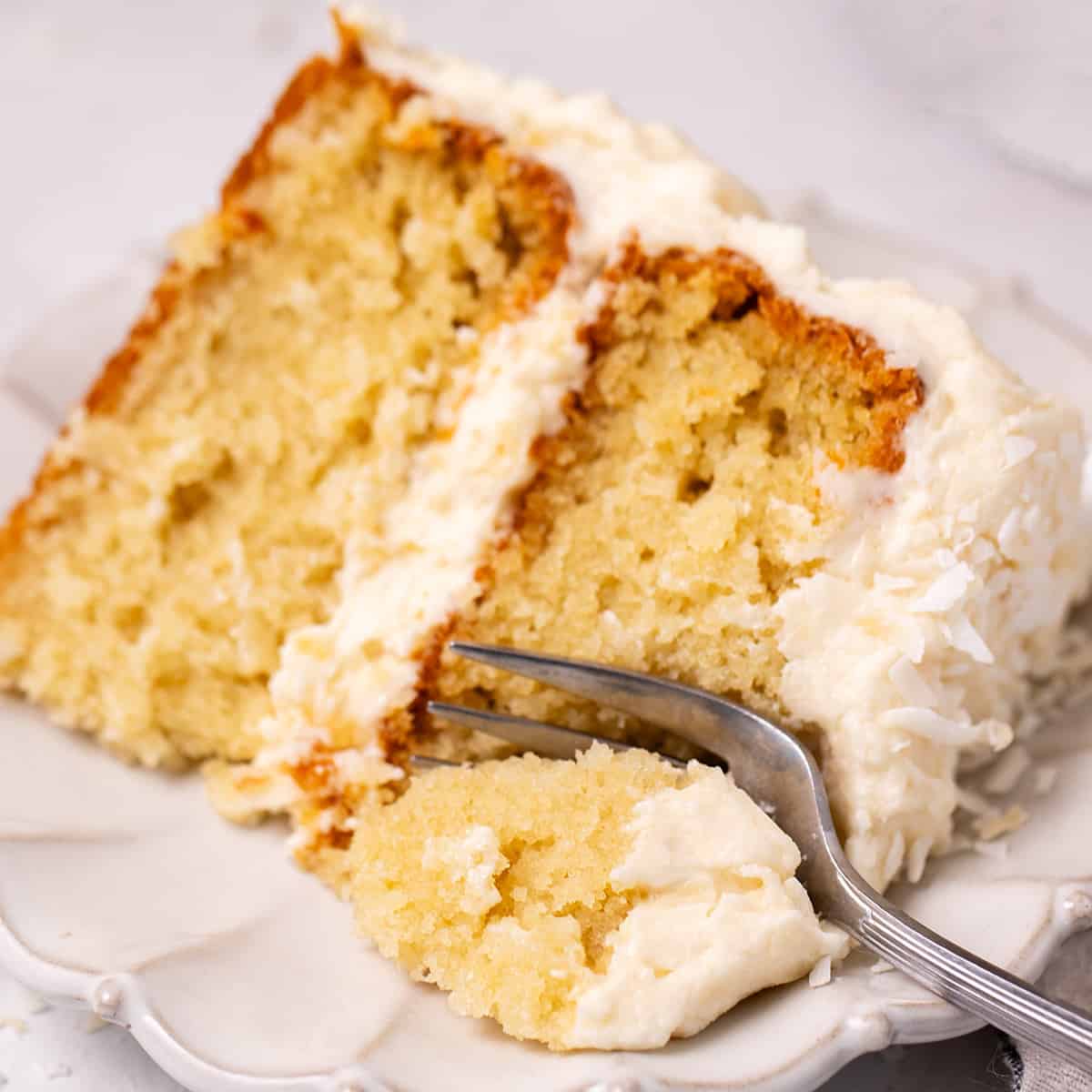 a fork taking a bite out of a slice of Coconut Cake on a plate