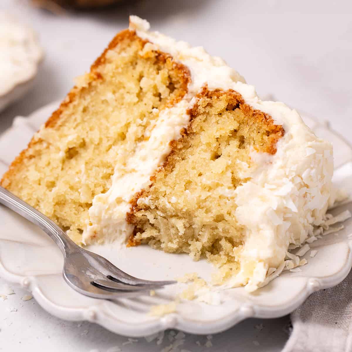 a slice of Coconut Cake on a plate with a fork and a bite taken out of it